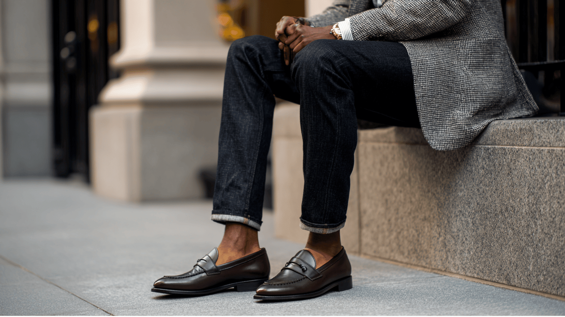 A man sits on a ledge wearing brown loafers and a blazer showing an outfit suited for evening plans and social time