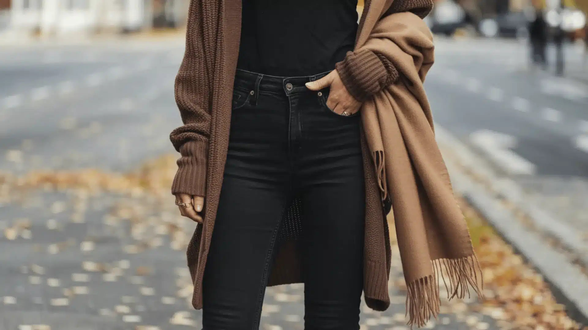 _A woman dressed in black jeans and a brown cardigan, posing in a relaxed manner