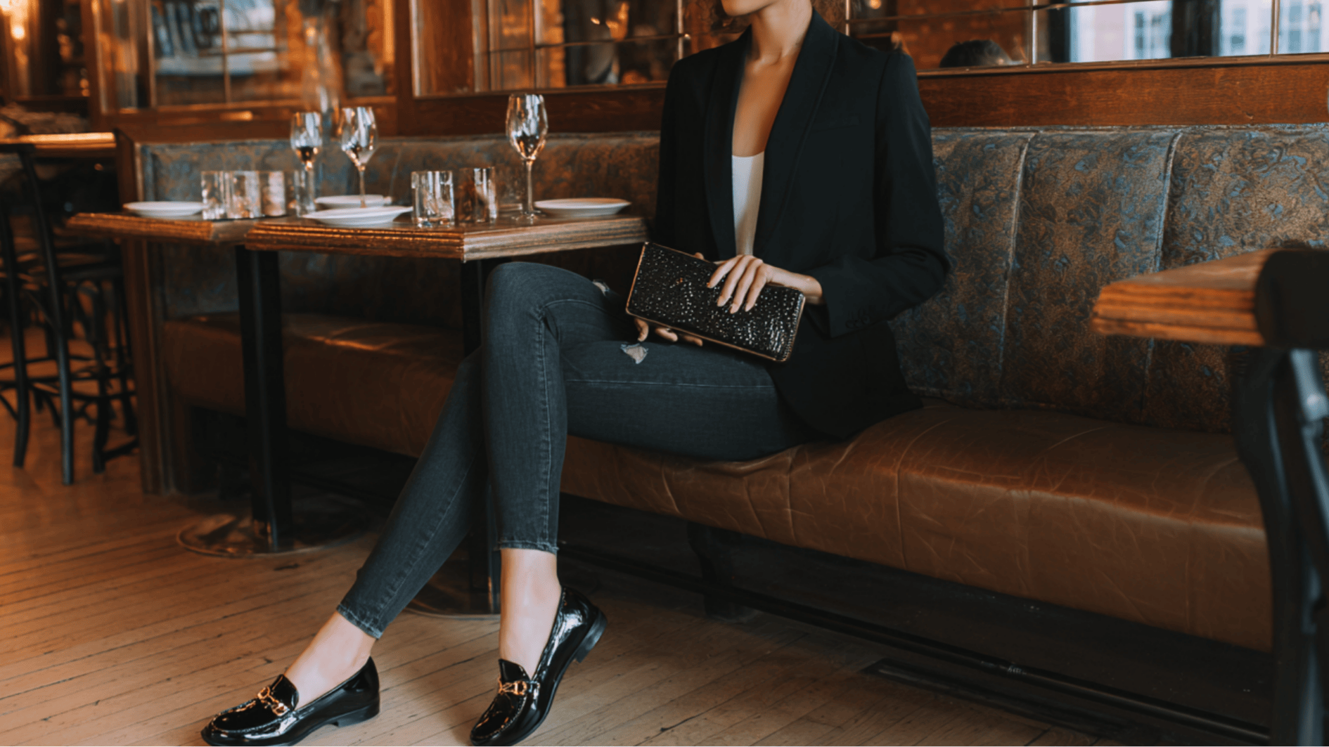 A woman wearing a fitted blazer and black shoes sits on a bench showing a neat date night outfit with a clean put together look