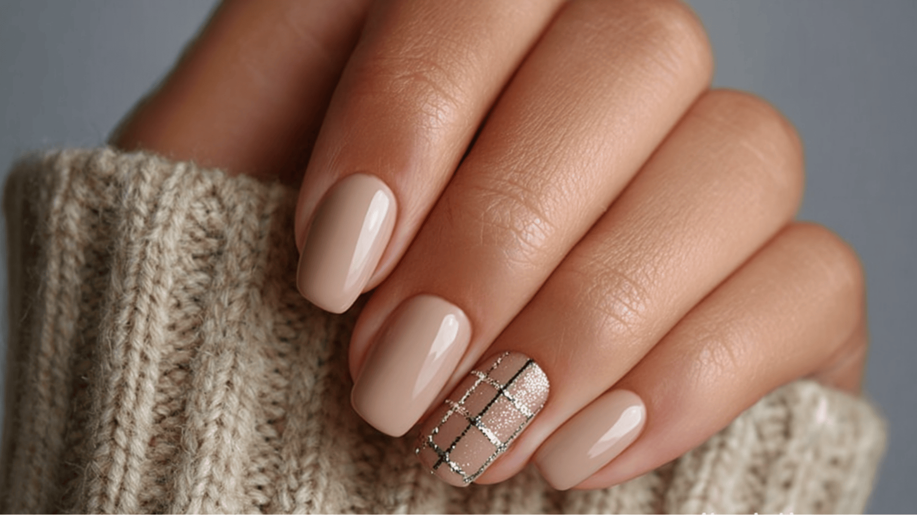 Close-up of a woman's hand showing spring nail trends with beige nails and one pastel accent nail, draped in a white sweater