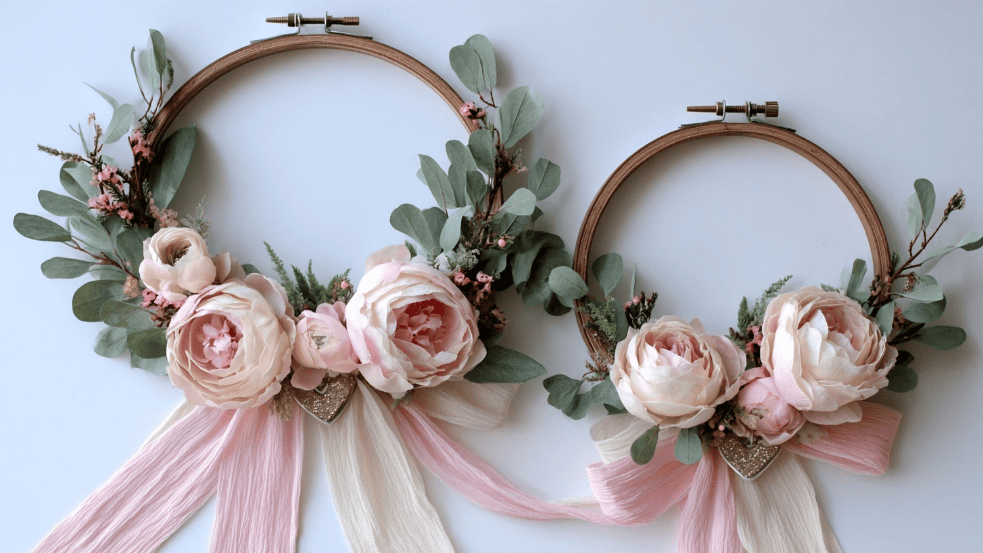 Two floral embroidery hoop wreaths featuring blush pink peonies, dusty green eucalyptus, and flowing silk ribbons against a light background.