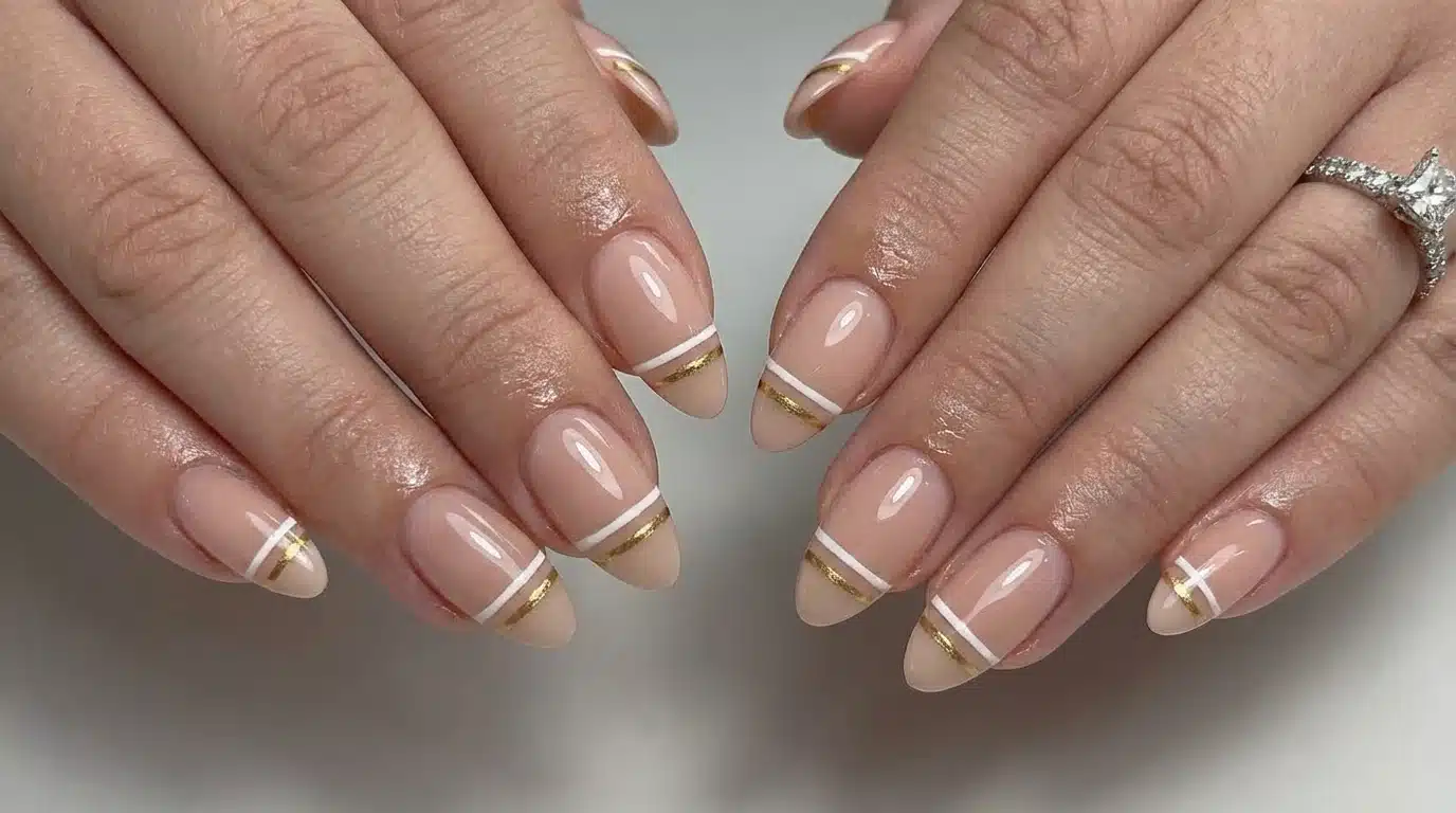 A close-up of a woman's hands showcasing nude nails with gold accents and a subtle double cuff design