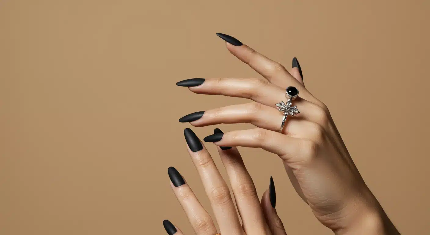 A pair of hands with black matte nails and stylish rings resting on a textured brown background offering a modern look