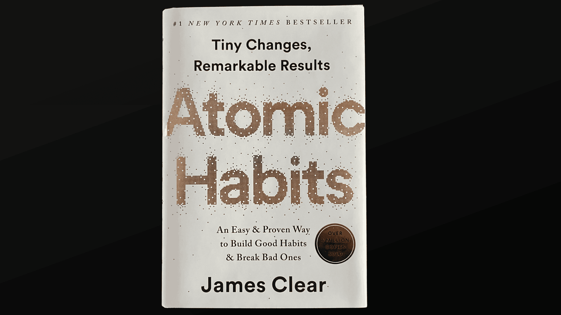 A white book cover titled Atomic Habits by James Clear sits on a black surface with text on how to organize your life