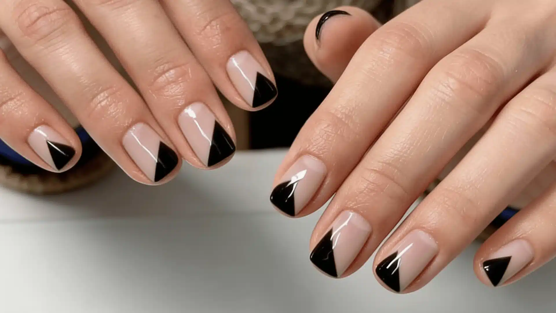 A woman with black and nude nails holds a black and nude manicure featuring half black negative space design with gloss finish