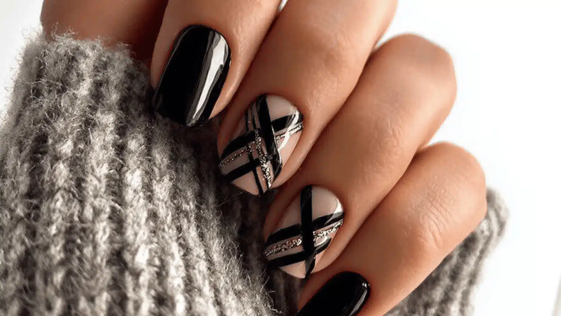 A woman's hand with black nails holds a nude base with black and gold striped manicure featuring diagonal black accents (1)