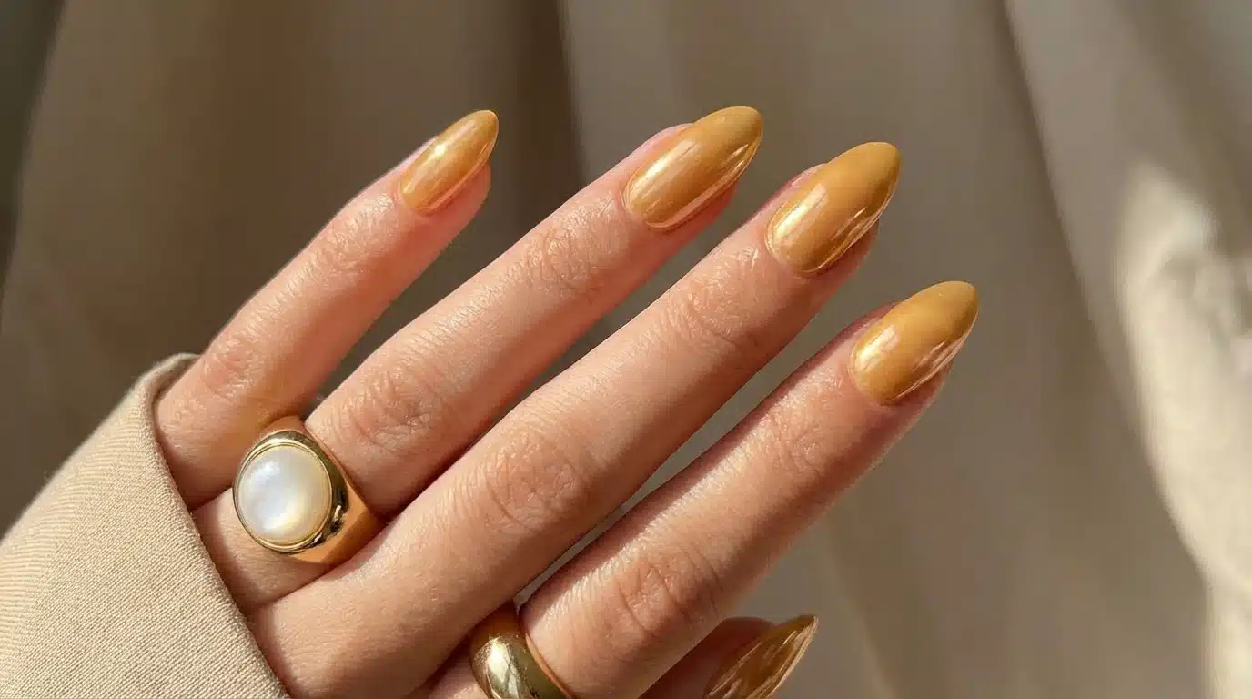 A woman's hand with yellow nails and rings, presenting a stylish warm honey glaze neutral nail look