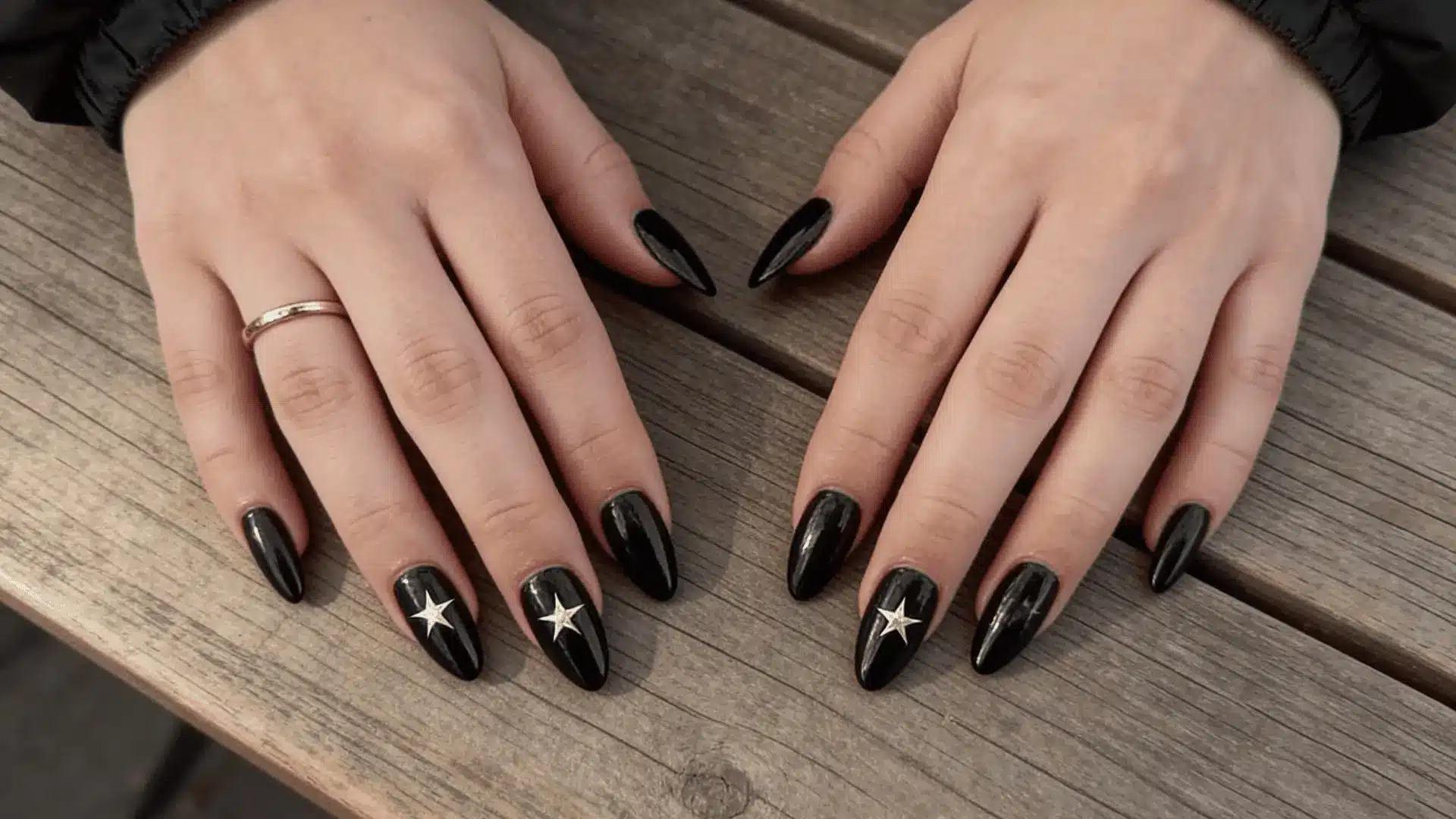 A woman's hands with black nails adorned with star decals, showcasing a striking black and star-themed nail design