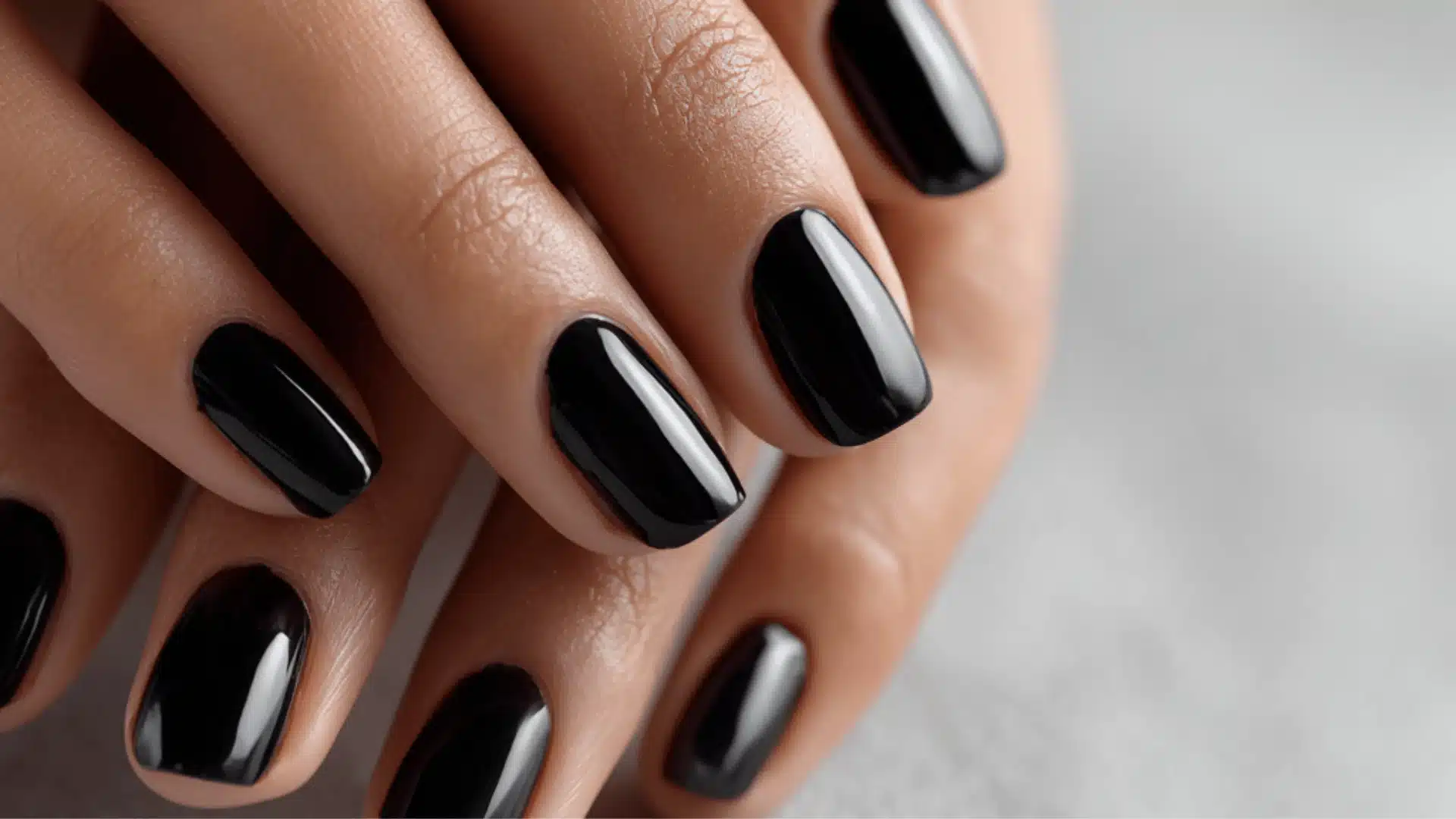 Glossy black nail polish on a woman's short nails, creating a sleek, polished look with a modern and refined appearance