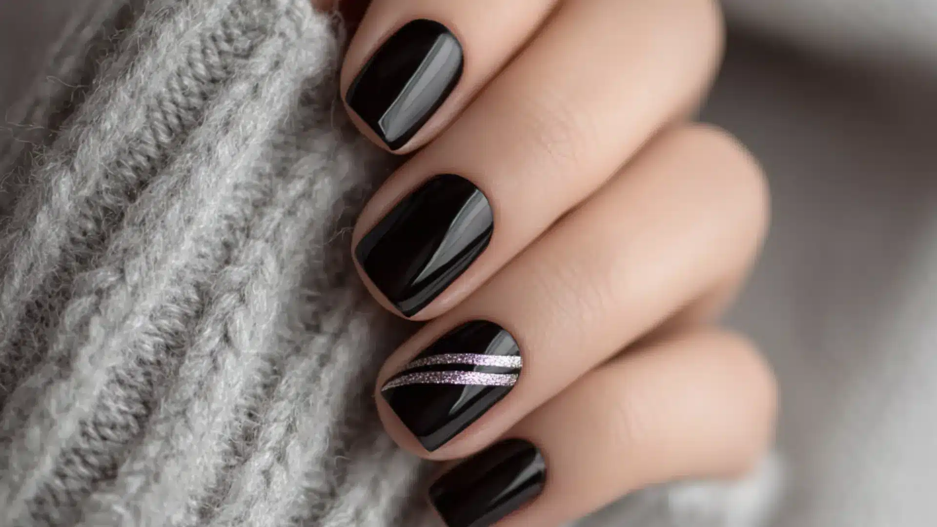 Short glossy black nail art featuring a silver diagonal stripe with glitter accents for a stylish look with grey sweater background