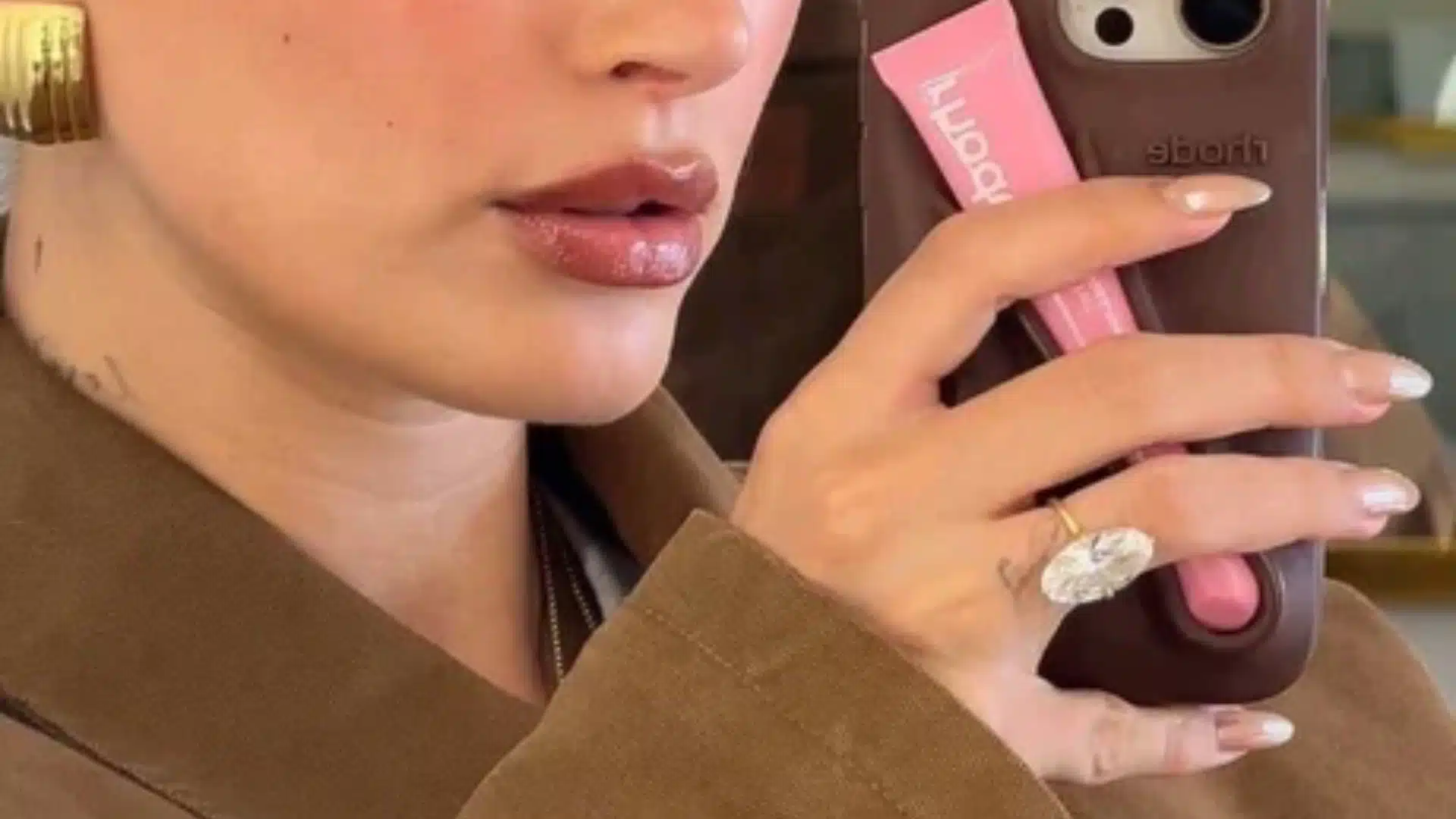 Close-up of hailey beiber with glossy lips showcasing a large oval diamond ring and French manicure nails