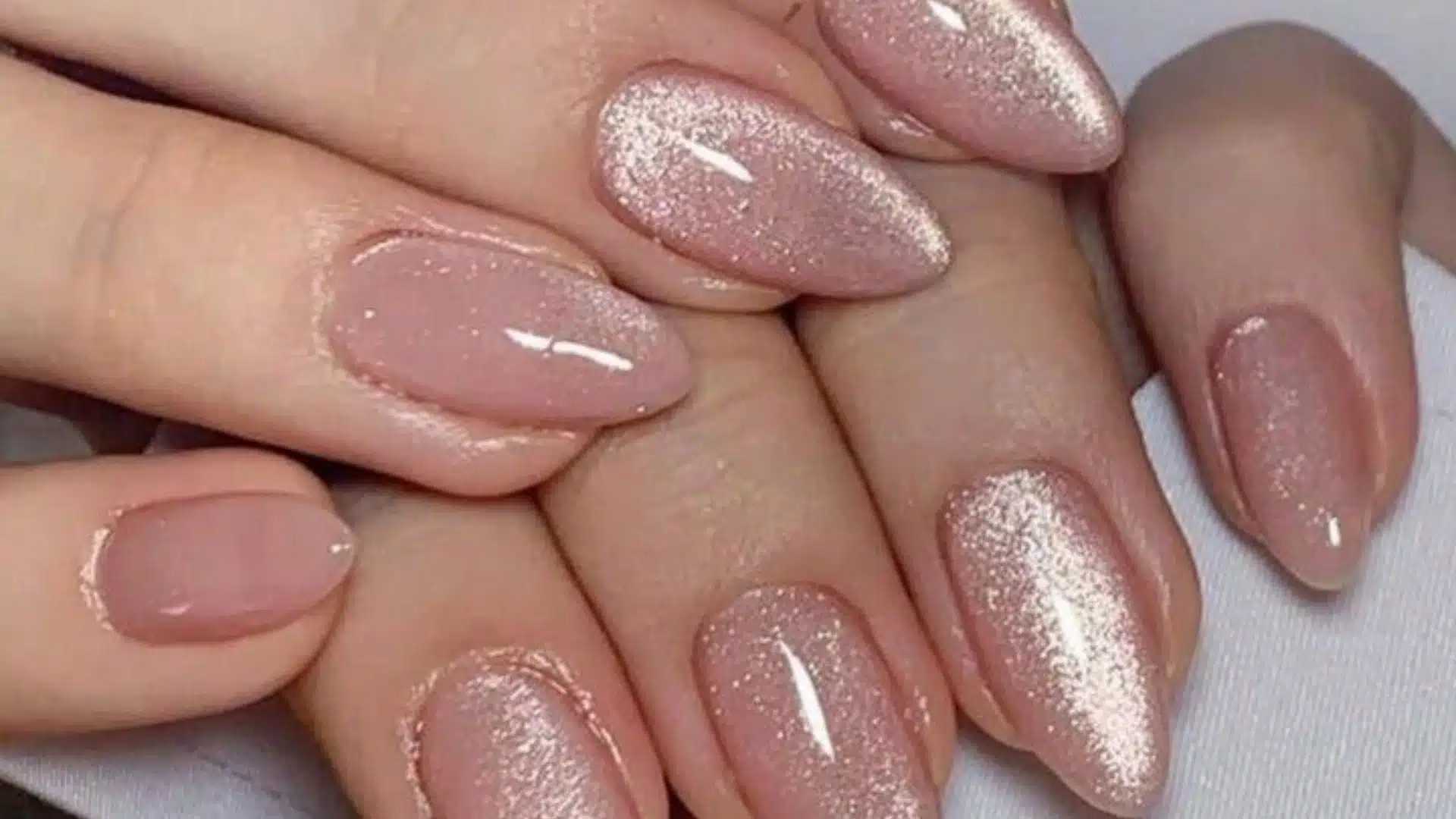 Close-up of manicured nails showing a mix of sheer pink glossy polish and sparkling rose gold cat-eye effect polish on almond-shaped extensions