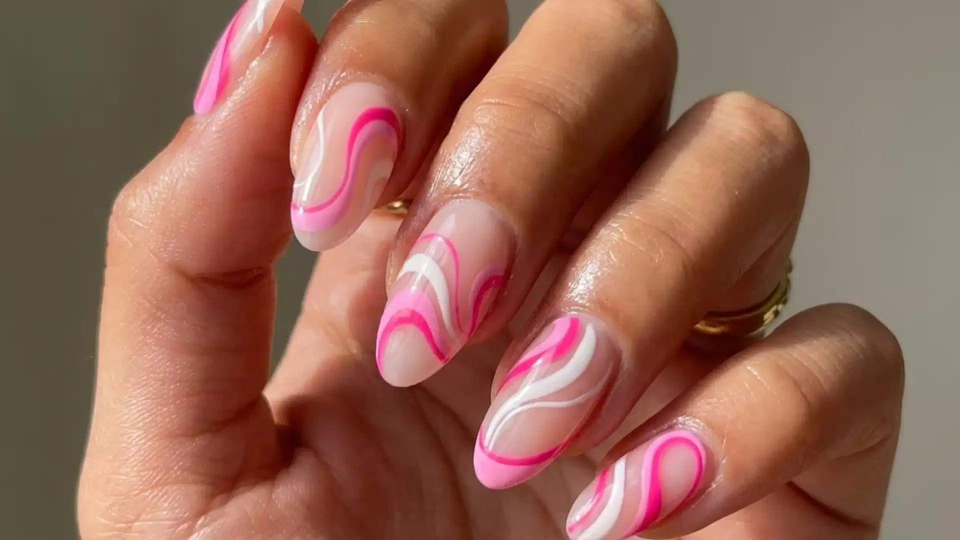 A close-up of a woman's hand showcasing pink and white swirl designs on her nails