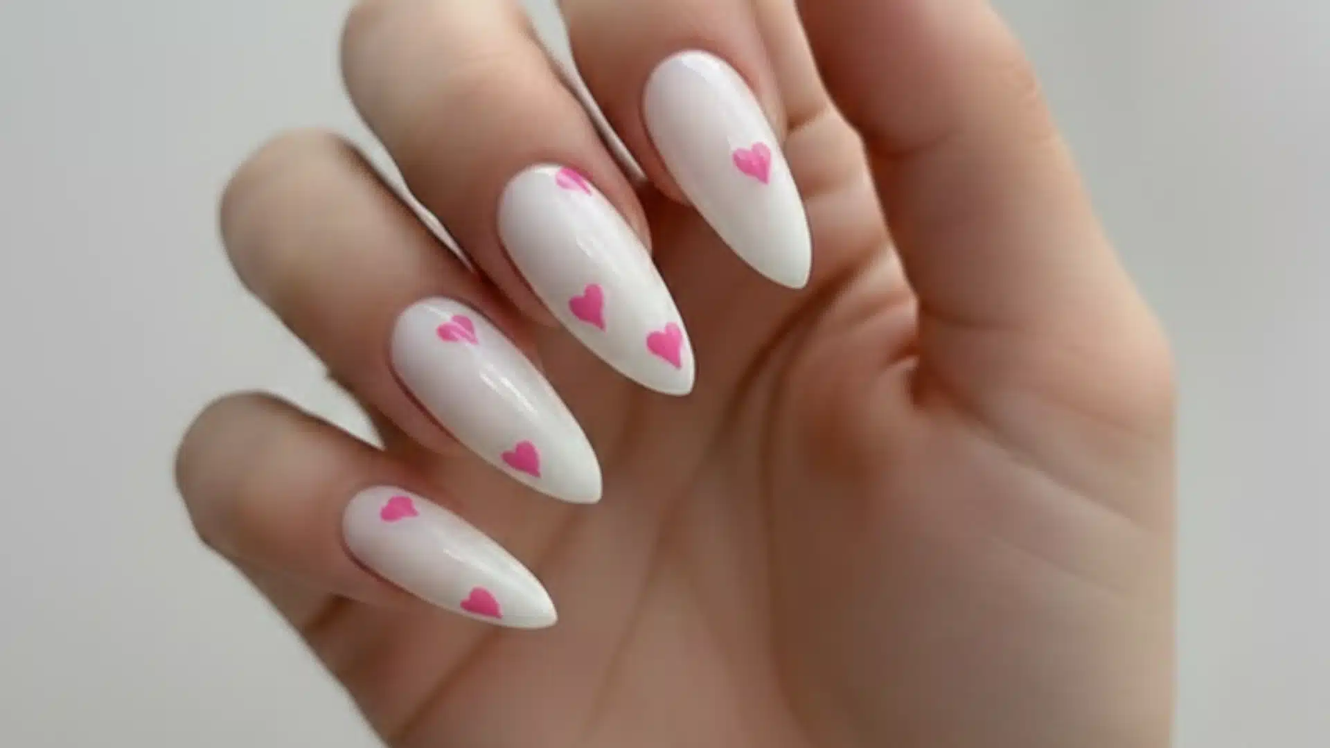 A close-up of a woman's hand with white nail base decorated with small pink hearts creating a playful and cute nail design