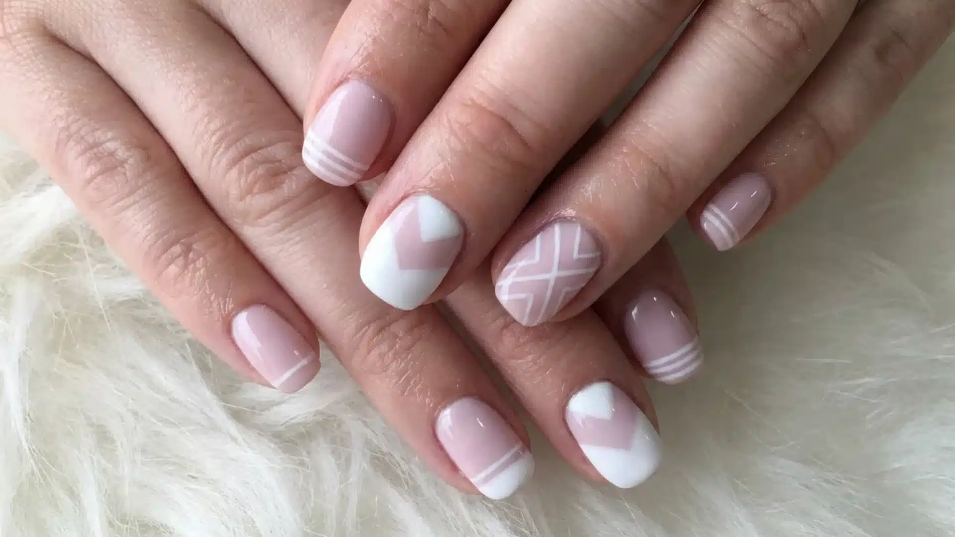 A woman's hand displaying pink and white geometric nails, highlighting a stylish manicure