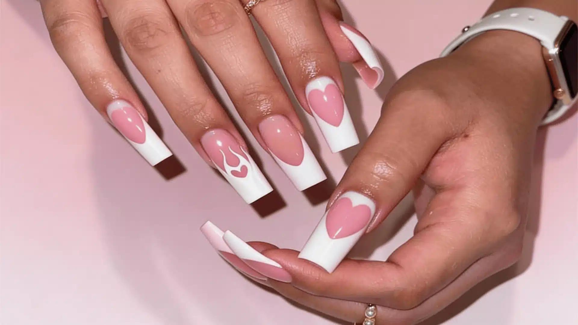 A woman's hand with pink white nails featuring a white heart flames design, showcasing a creative and bold nail art style