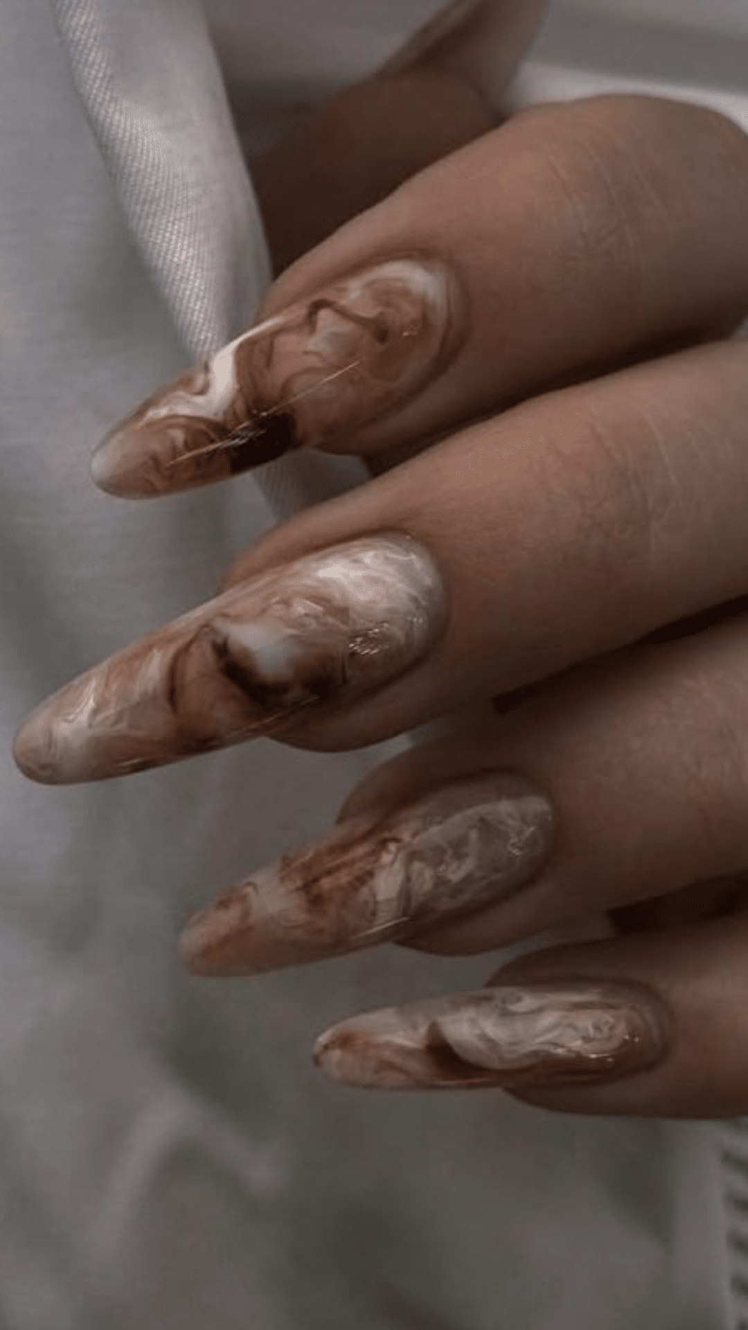 Almond-shaped nails with a marbled blend of brown and cream, creating an artistic classy brown nail designs look.