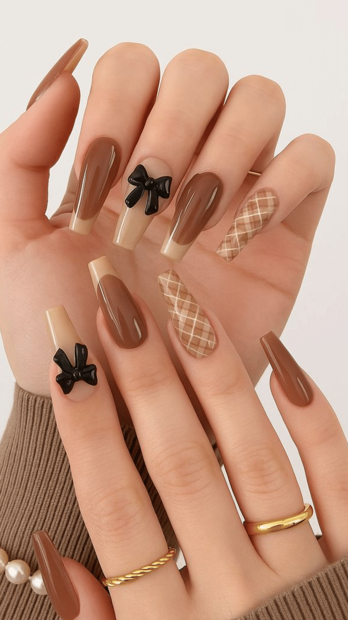 Long coffin-shaped nails in warm brown tones, accented with black bows and beige plaid designs