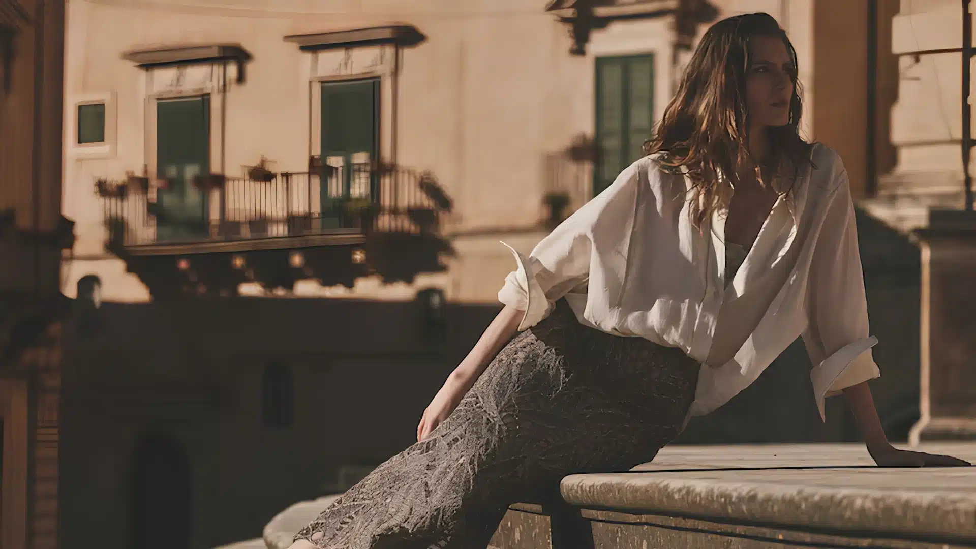 Woman in Brunello Cucinelli's white blouse and patterned skirt sitting on stone steps