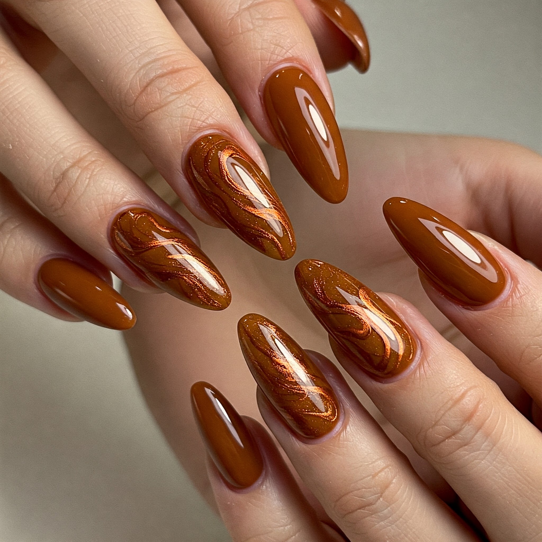 Close-up of hands with long, almond-shaped nails painted in glossy brown.