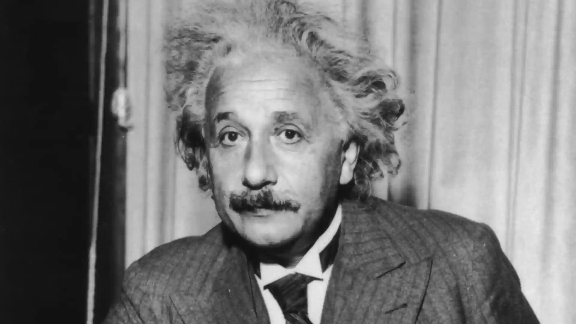Albert Einstein with his signature unruly hair, mustache, and suit, looking directly at the camera.