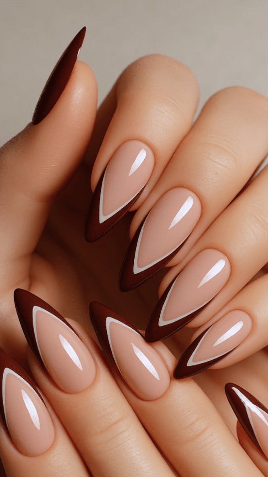 Almond-shaped nails with a nude base and sharp dark brown tips outlined in white, creating a bold look.