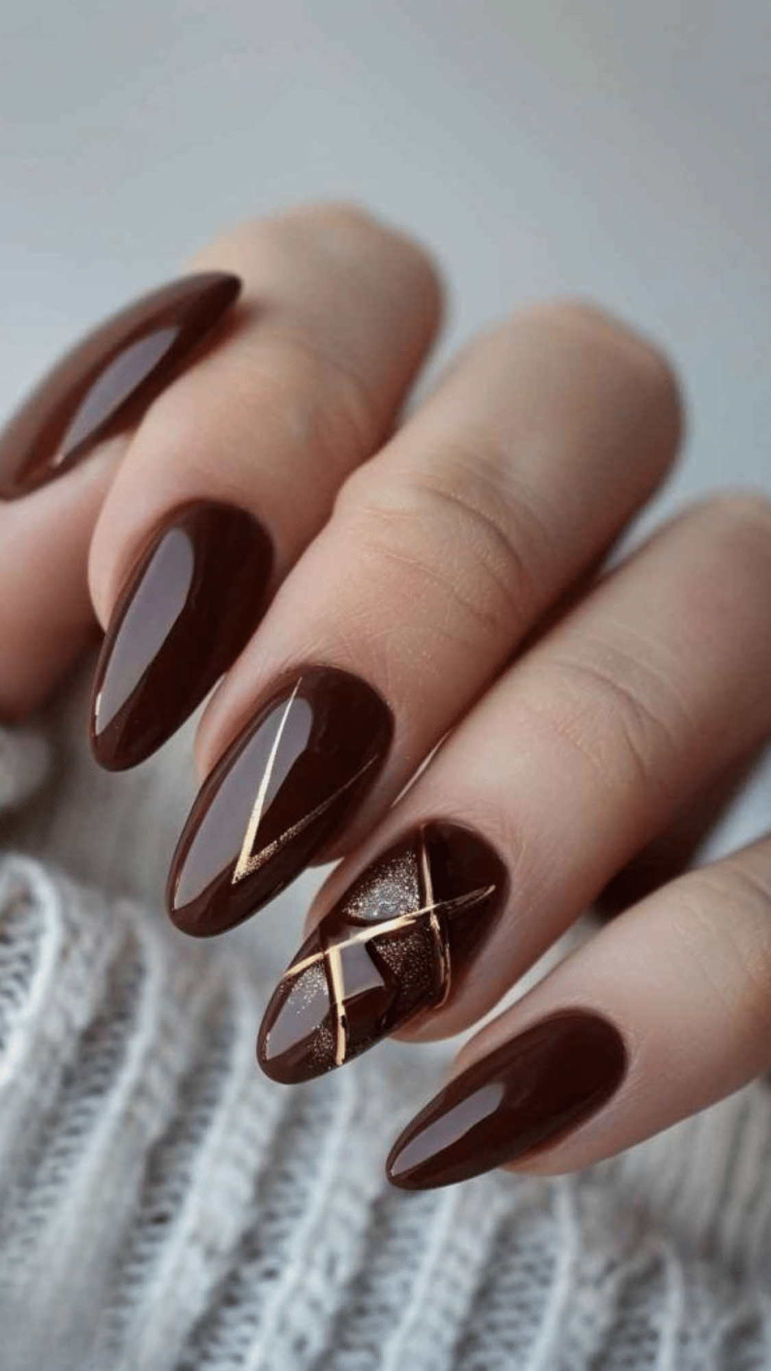 Glossy almond-shaped nails in deep chocolate brown with gold geometric accents, creating a chic classy brown nail designs look.