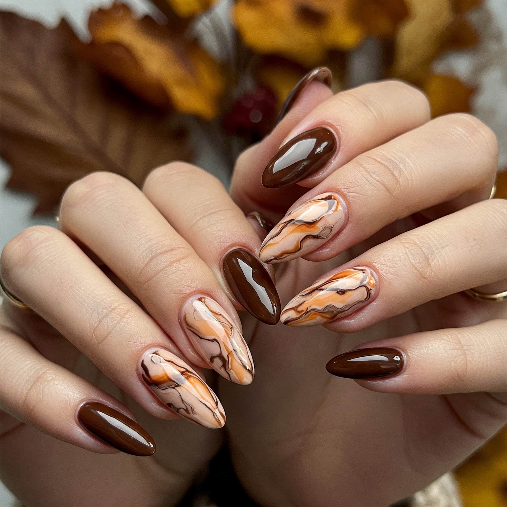 A woman with brown and white nails holds a brown and white marble manicure, showcasing her stylish nail art