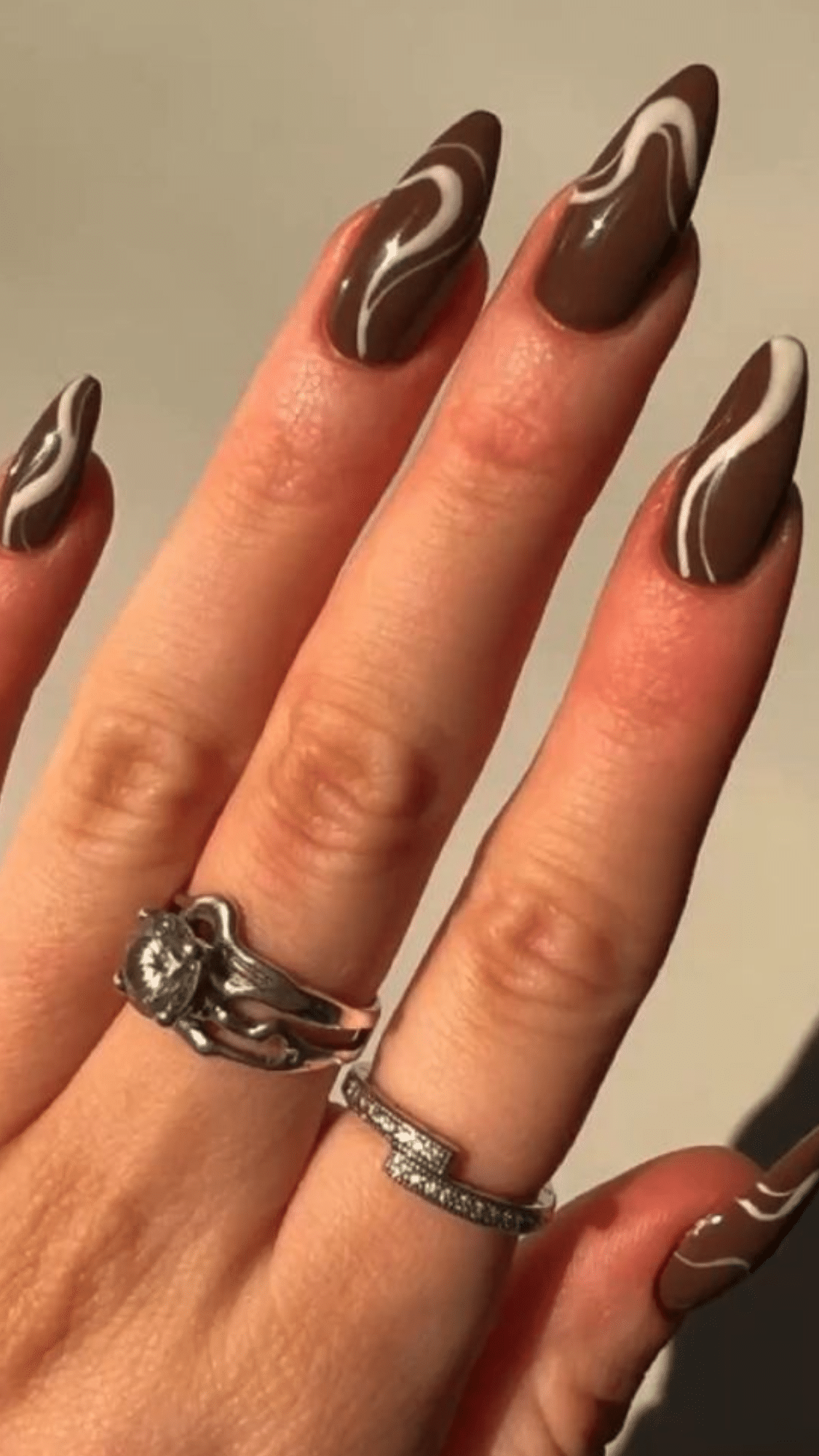 Glossy almond nails in rich brown with white swirl accents, perfect for a bold and trendy classy brown nail designs look.