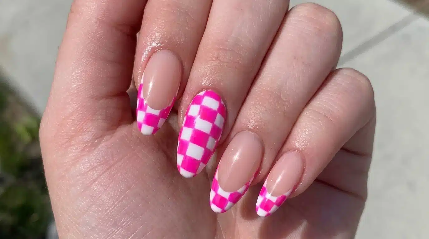 Close up of a person's hand displaying a pink and white checkerboard nail design, highlighting a trendy nail art style