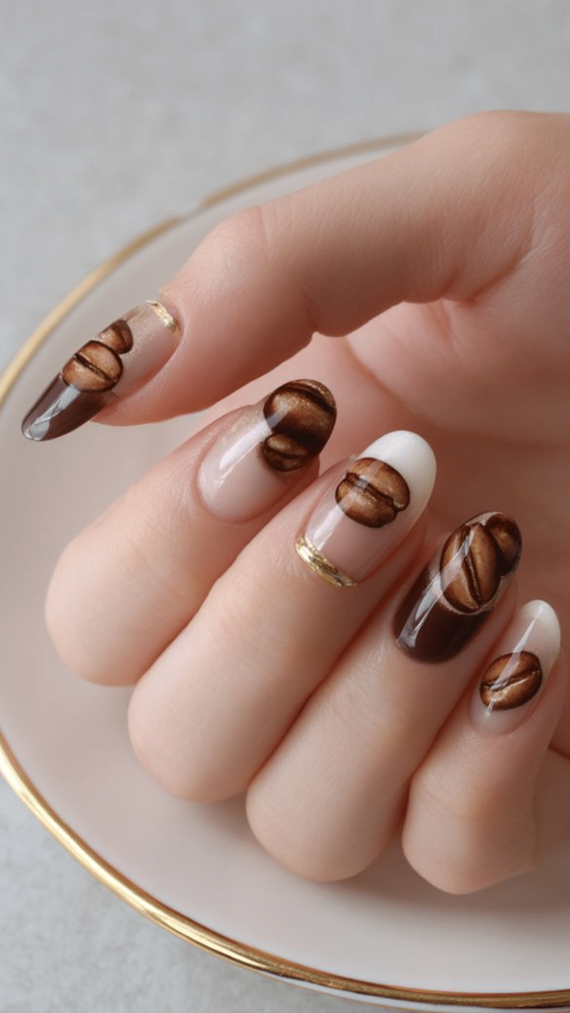 Almond nails with a clear base, accented by realistic brown coffee bean designs and gold tips, perfect for a playful classy brown nail designs look.