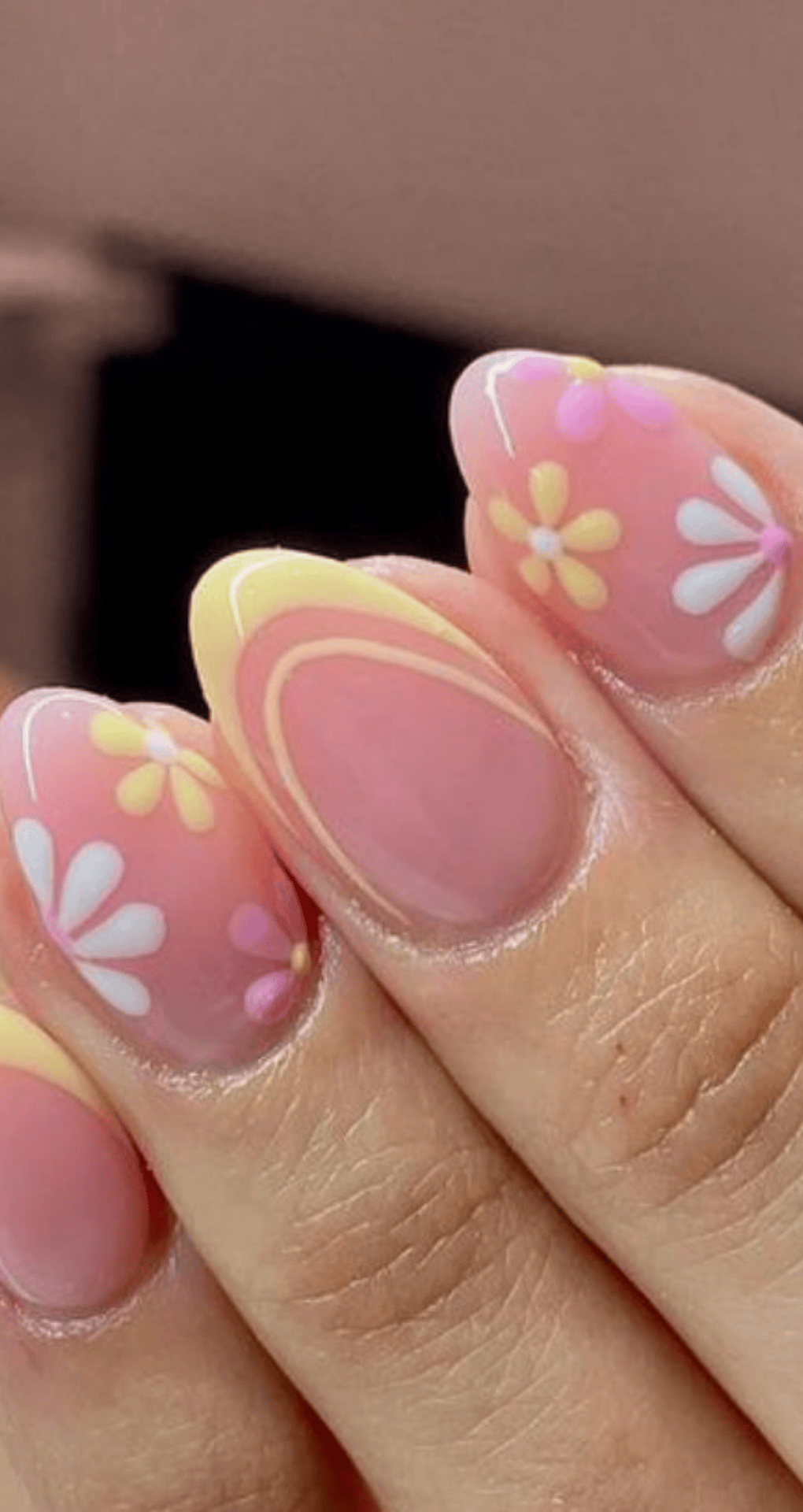 Oval nails with pink base featuring white and yellow flowers and yellow and white swirls on middle nail