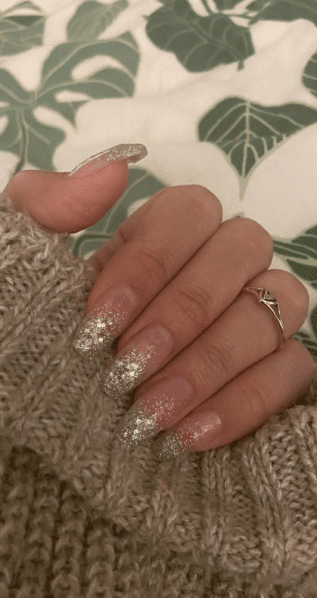 Almond nails with nude base fading into dense silver glitter at tips with cozy sweater background