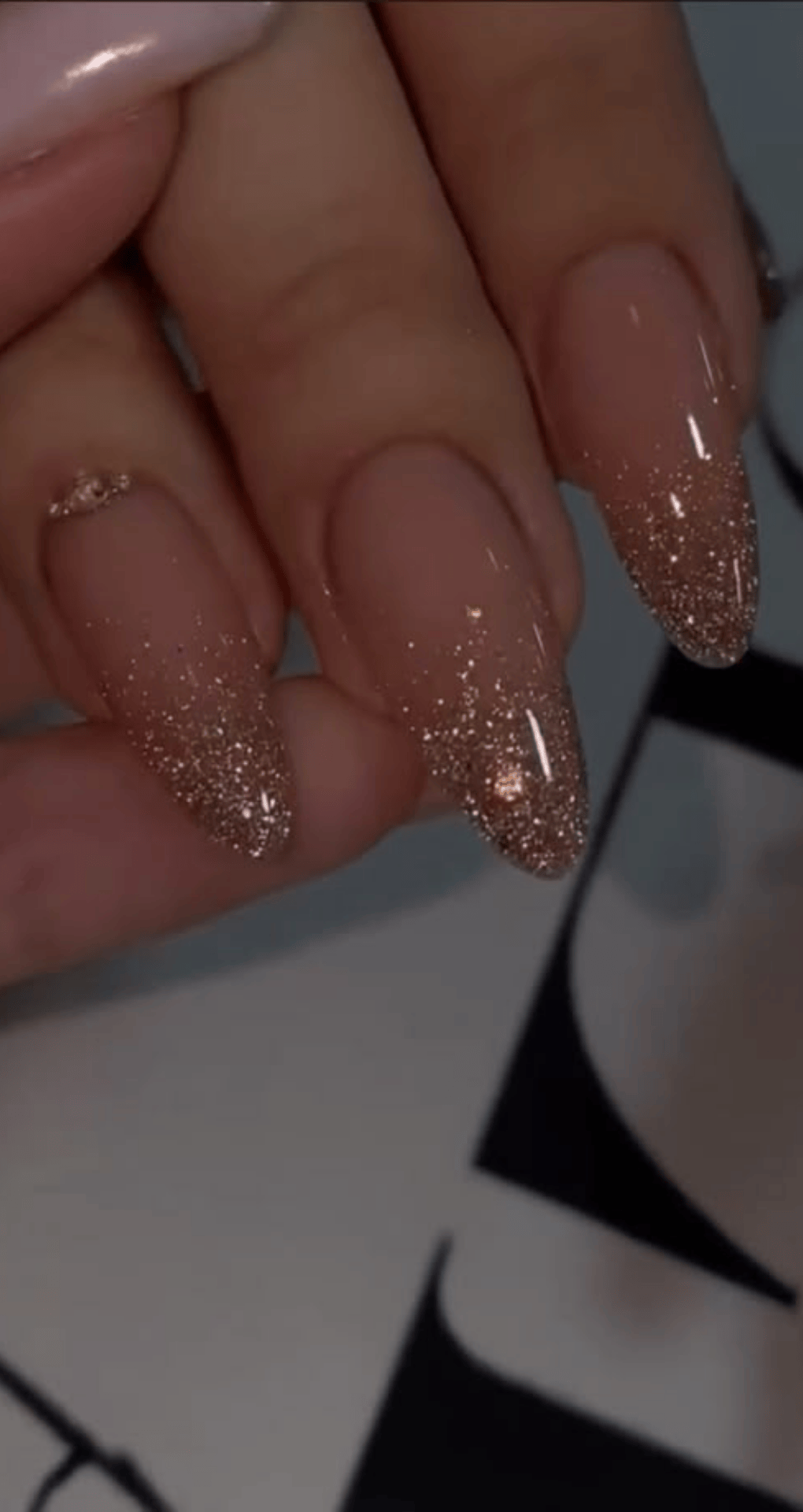 Almond nails with nude base fading into rose gold glitter at the tips for a sparkling look