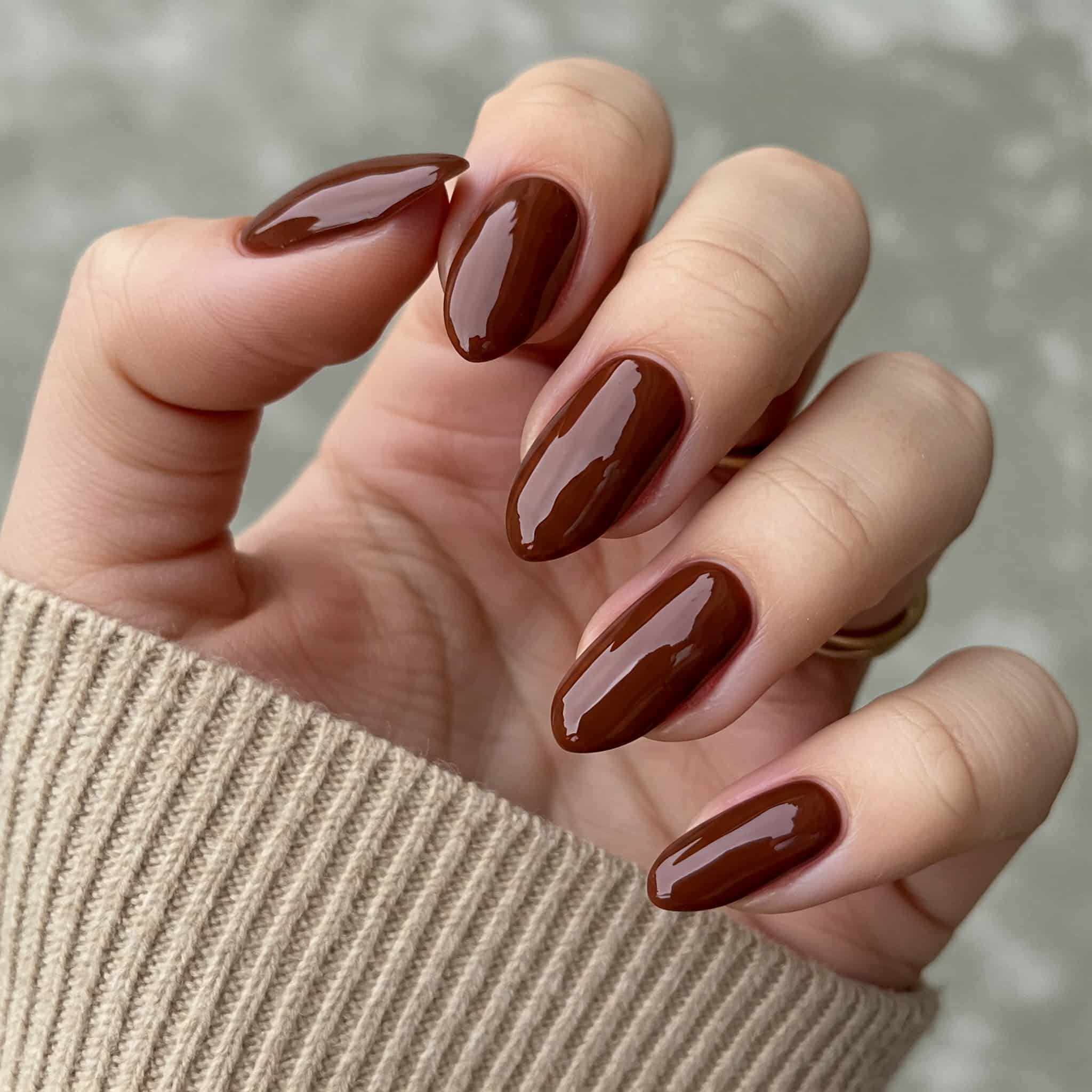 A close-up of a woman's hand gripping a bottle of brown nail polish, showcasing the polish's rich color