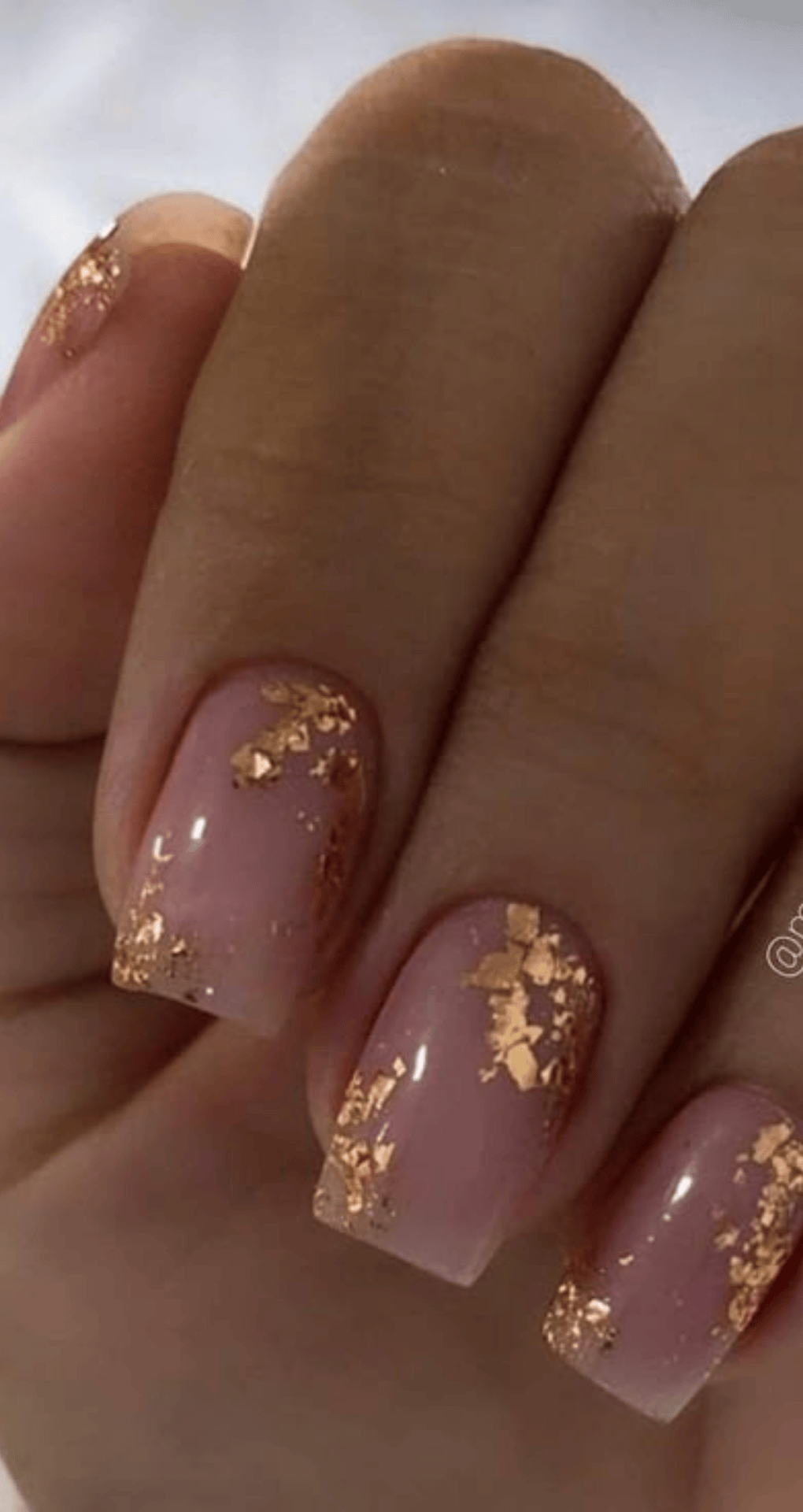 Square nails painted light pink with scattered metallic gold leaf on tips and edges