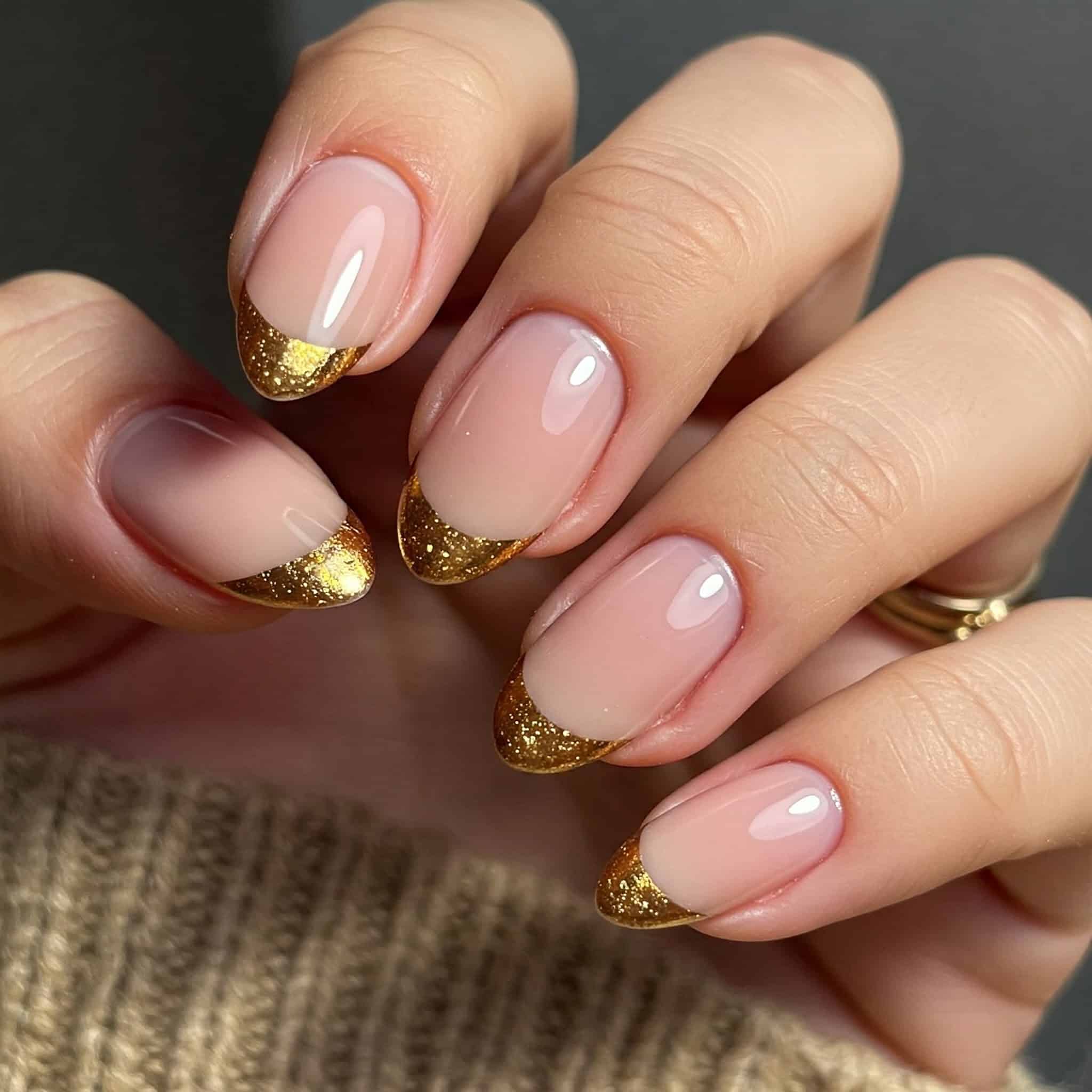 A close-up of a woman's hand showcasing gold nails paired with a pink manicure