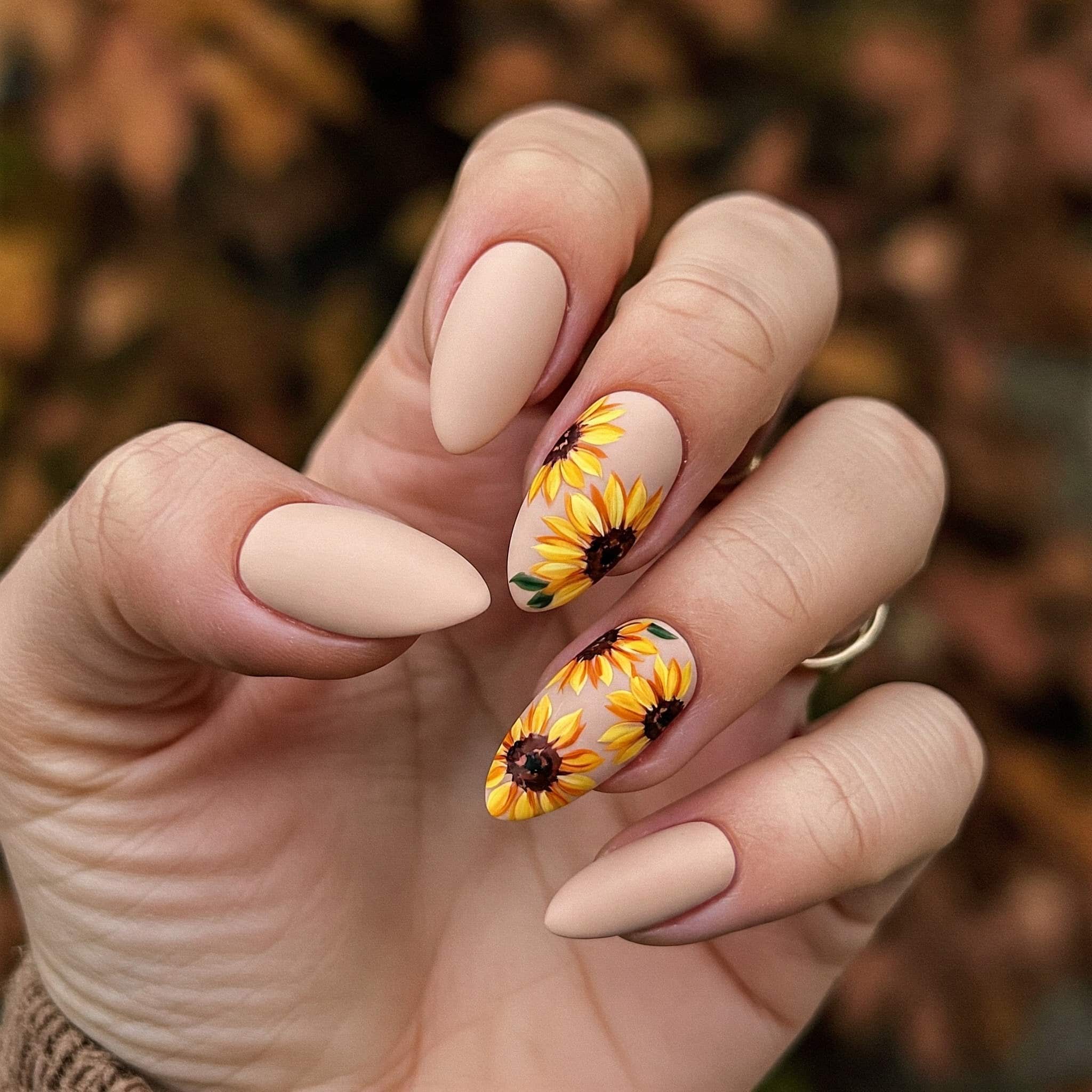 A close-up of vibrant sunflower nail art designs featuring yellow petals and green accents on a neutral background.