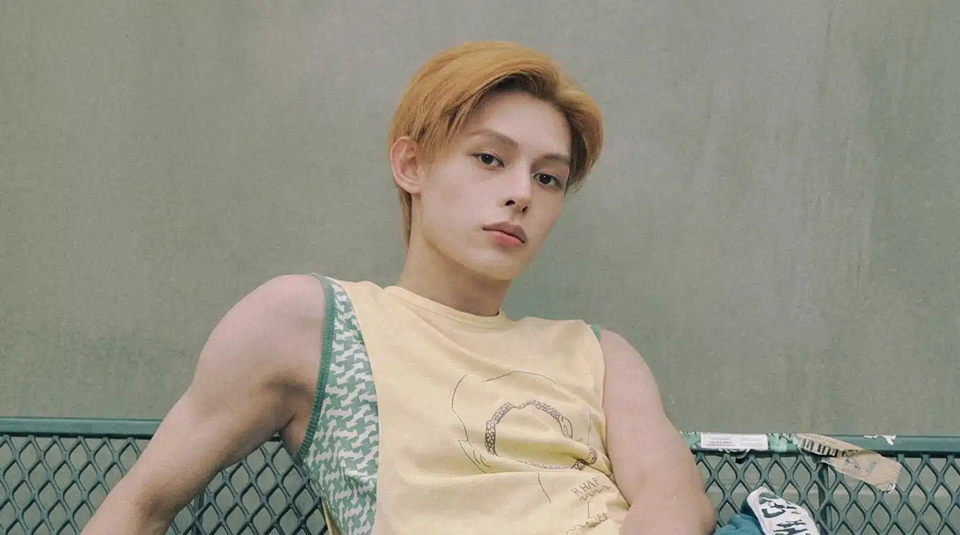 James posing on a bench in a sleeveless cream top, showcasing his stylish visuals and confident presence in a photoshoot.