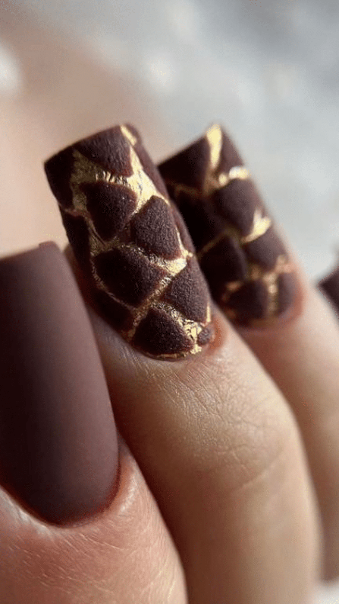 Square-shaped nails in matte chocolate brown with textured gold web accents