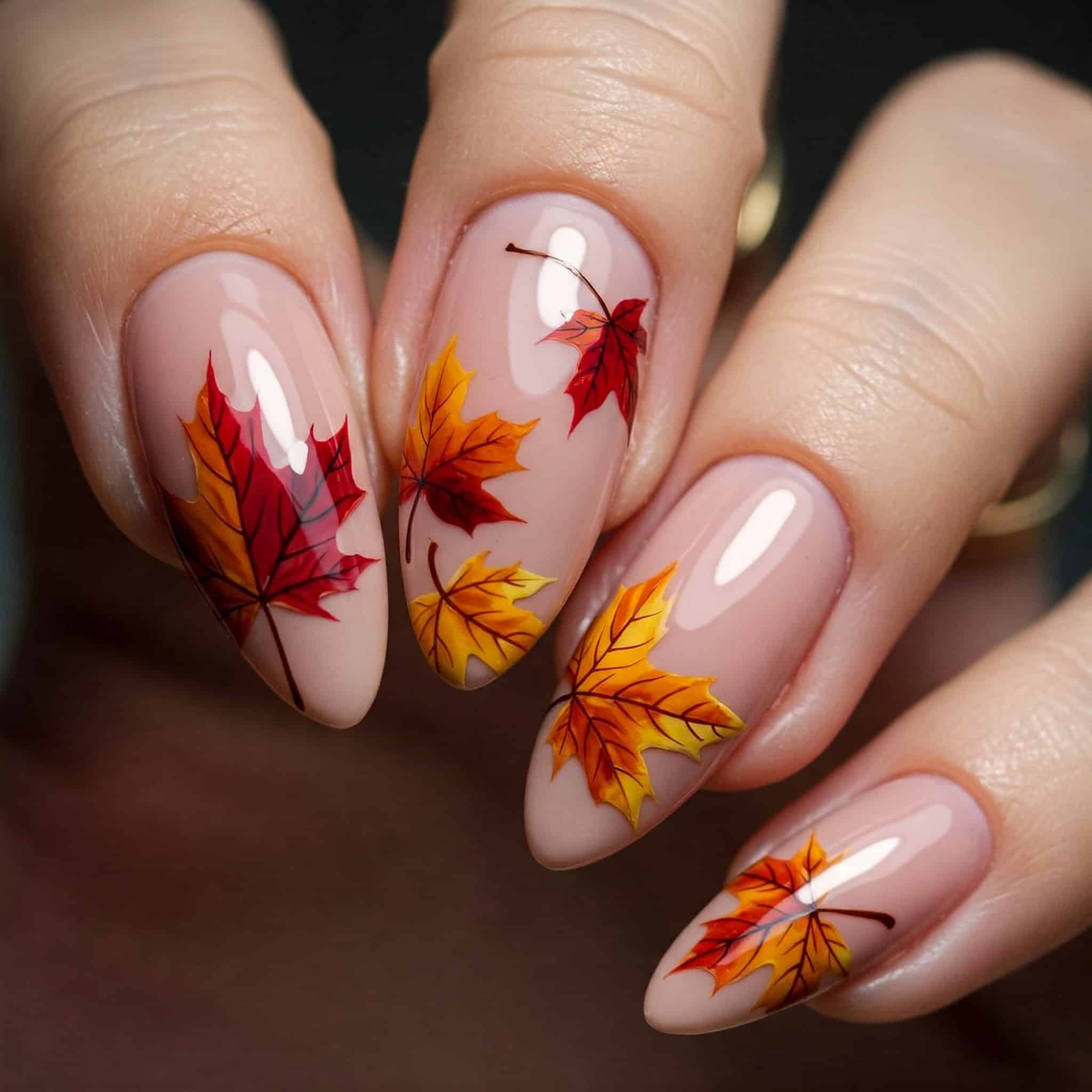 Close-up of a hand with almond-shaped nails painted in nude polish, adorned with vibrant autumn leaf designs in red, orange, and yellow tones.