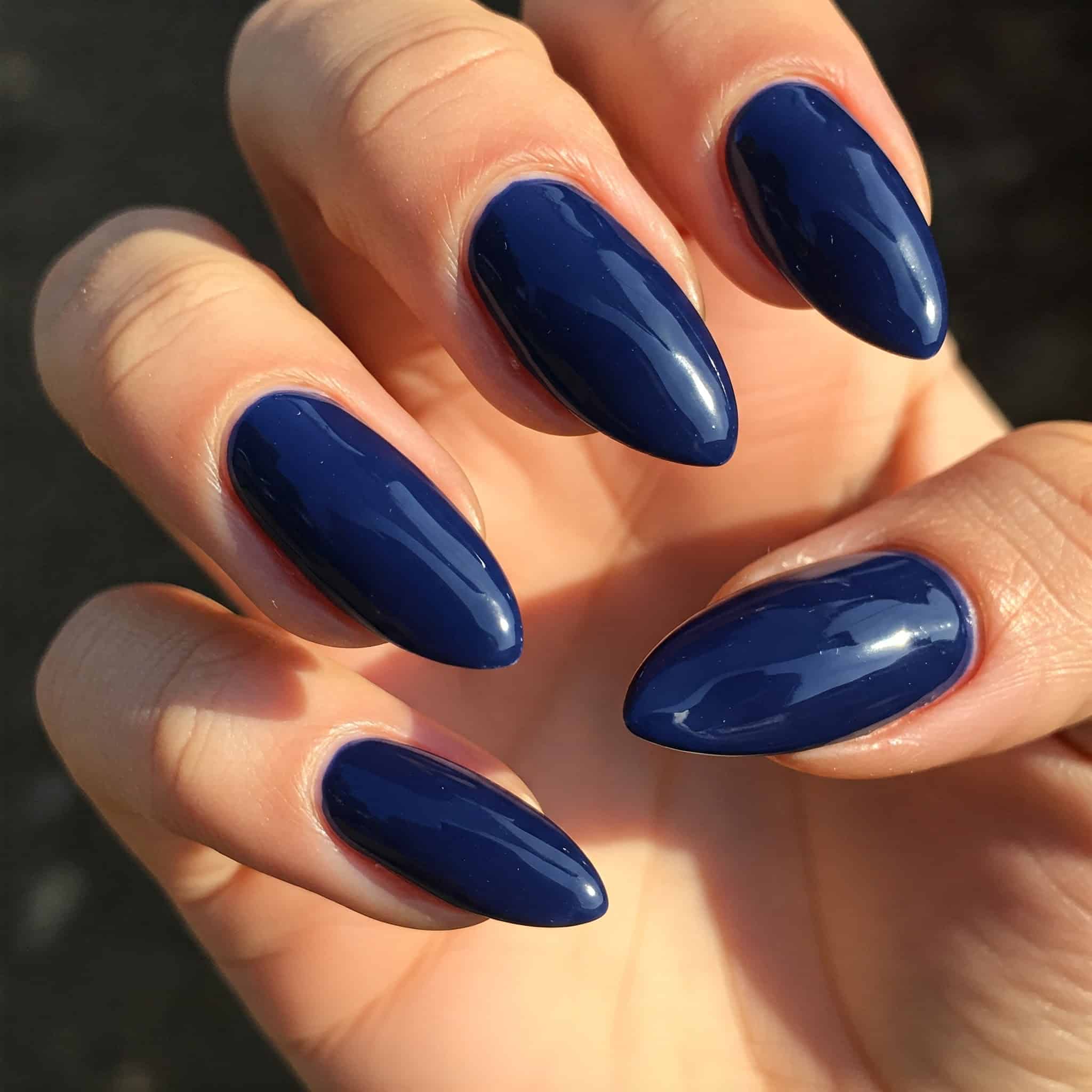 Close-up of a hand with long, almond-shaped nails painted in glossy dark blue.