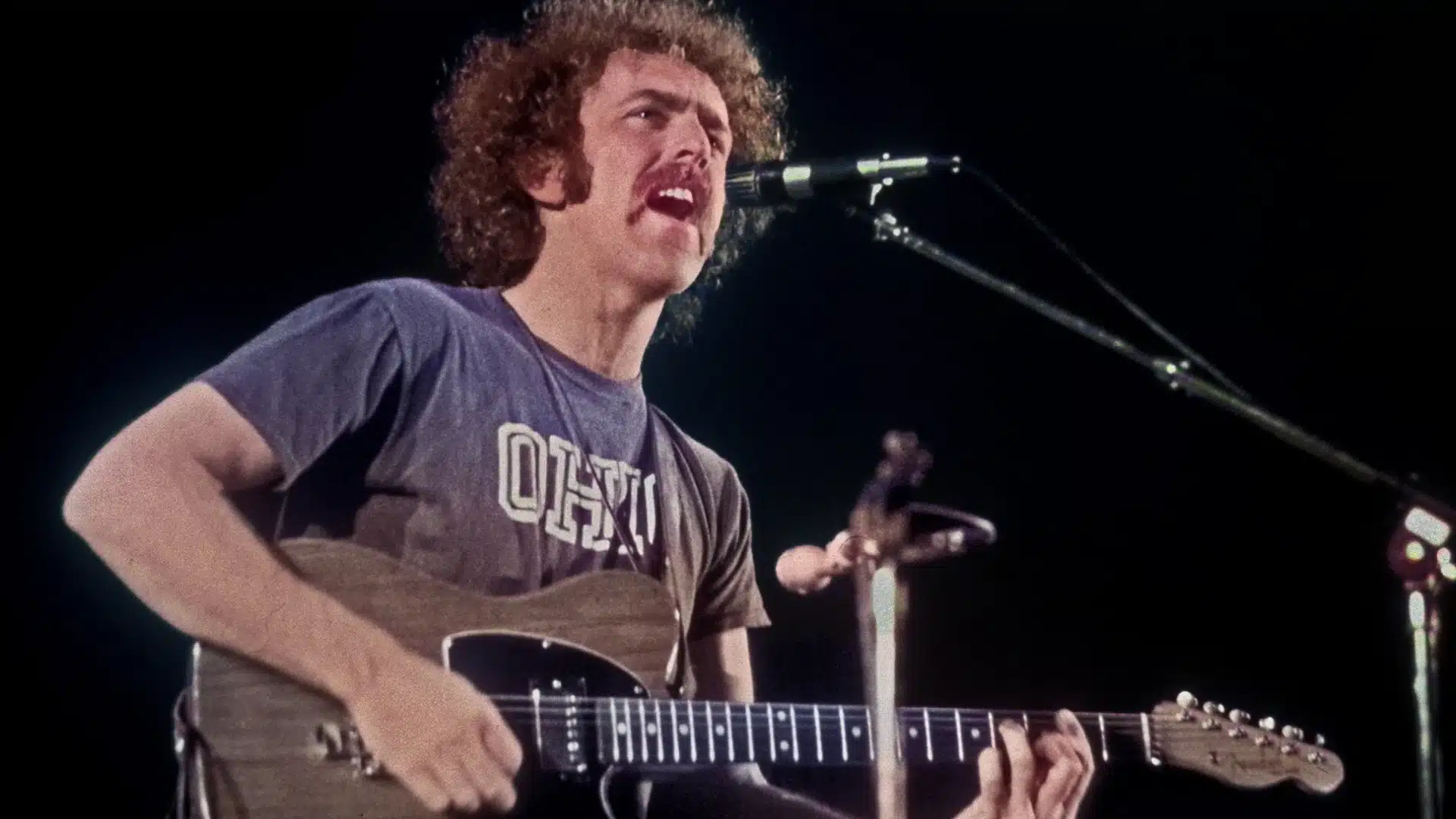 Bernie Leadon plays electric guitar and sings into a microphone on stage
