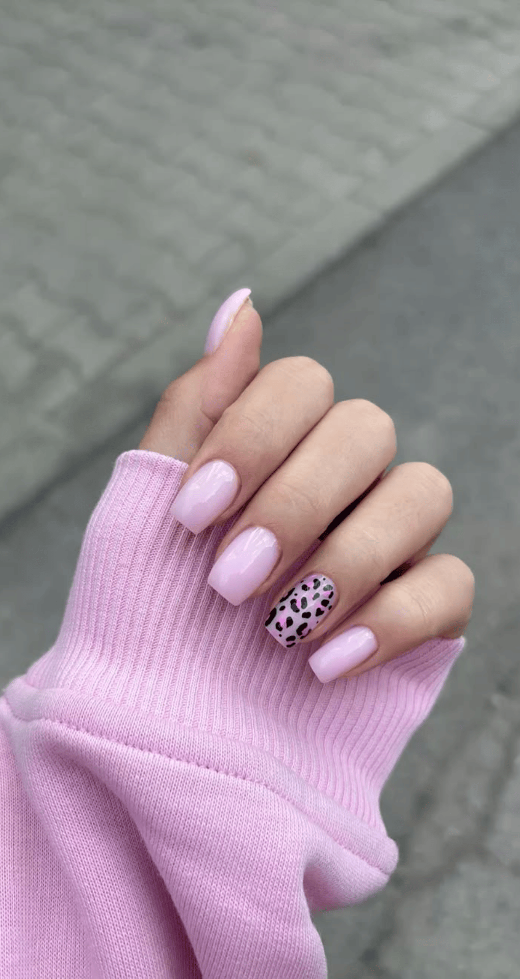Square nails painted light pastel pink with ring finger showing black leopard print accent