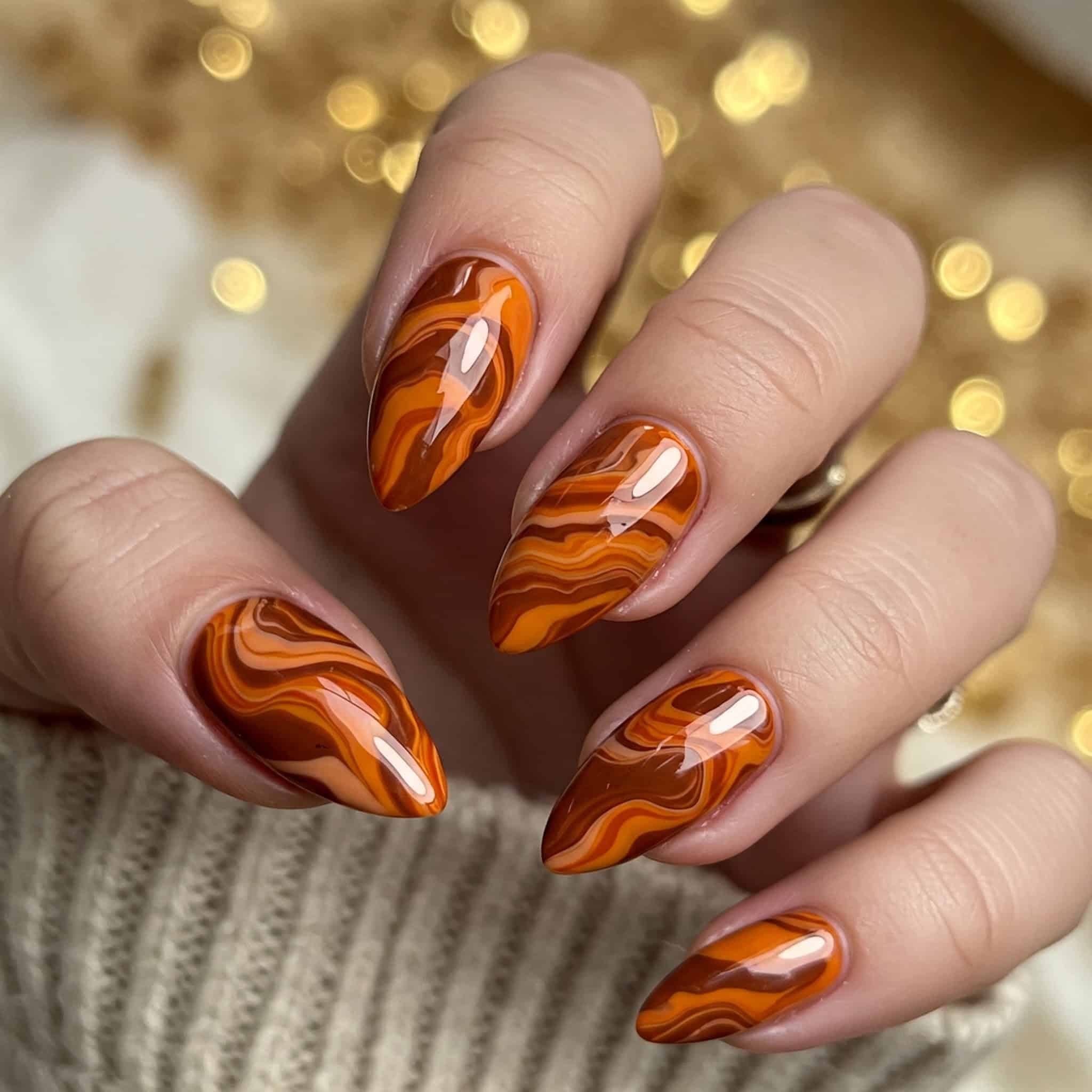 A woman's hand displaying vibrant orange and brown nail polish, highlighting her stylish manicure