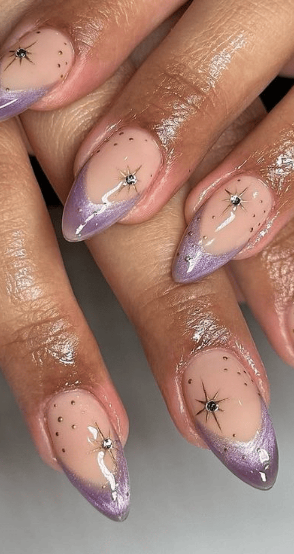 Pointed nails with nude base and purple gradient tips with small black star decals and dots