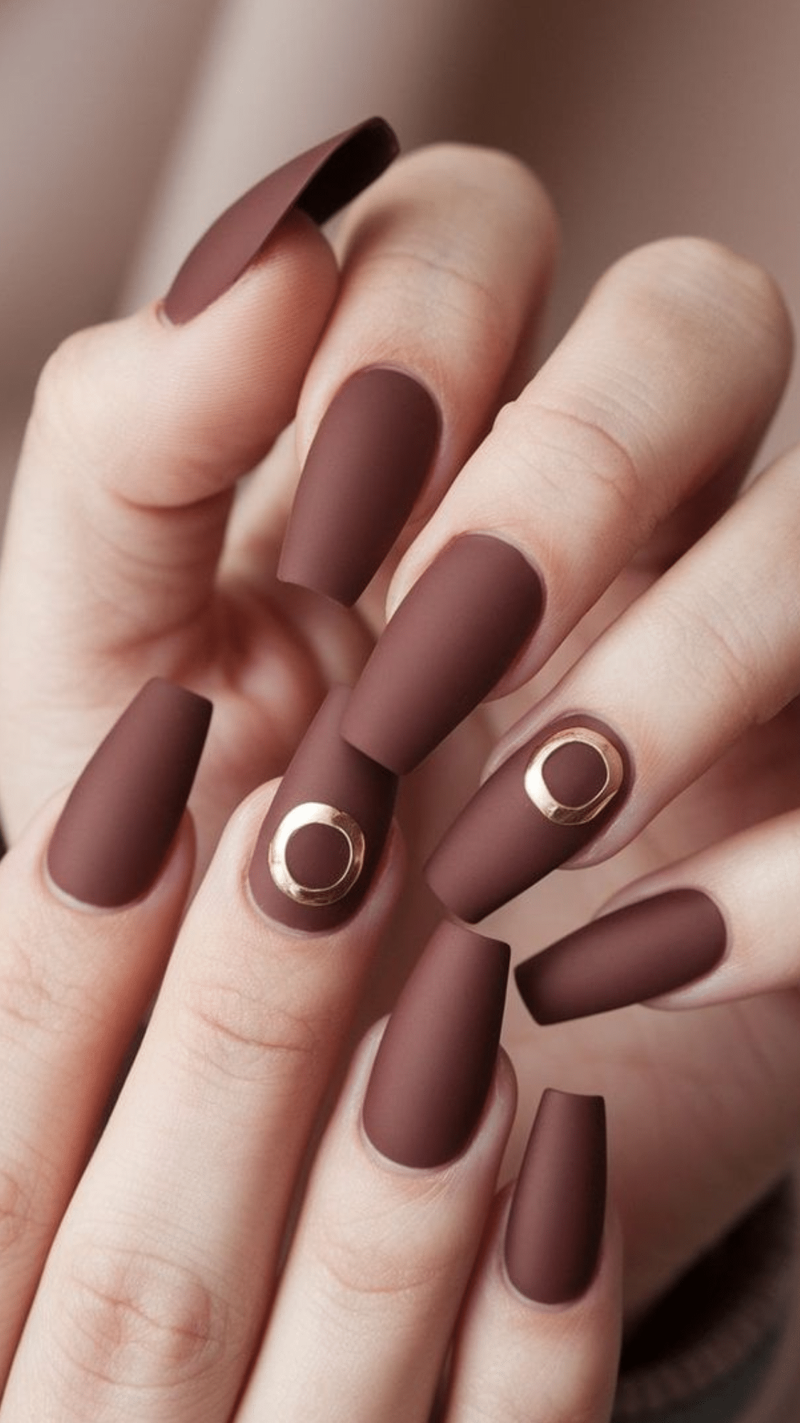 Matte coffin-shaped nails in rich chocolate brown, accented with small gold circle details.