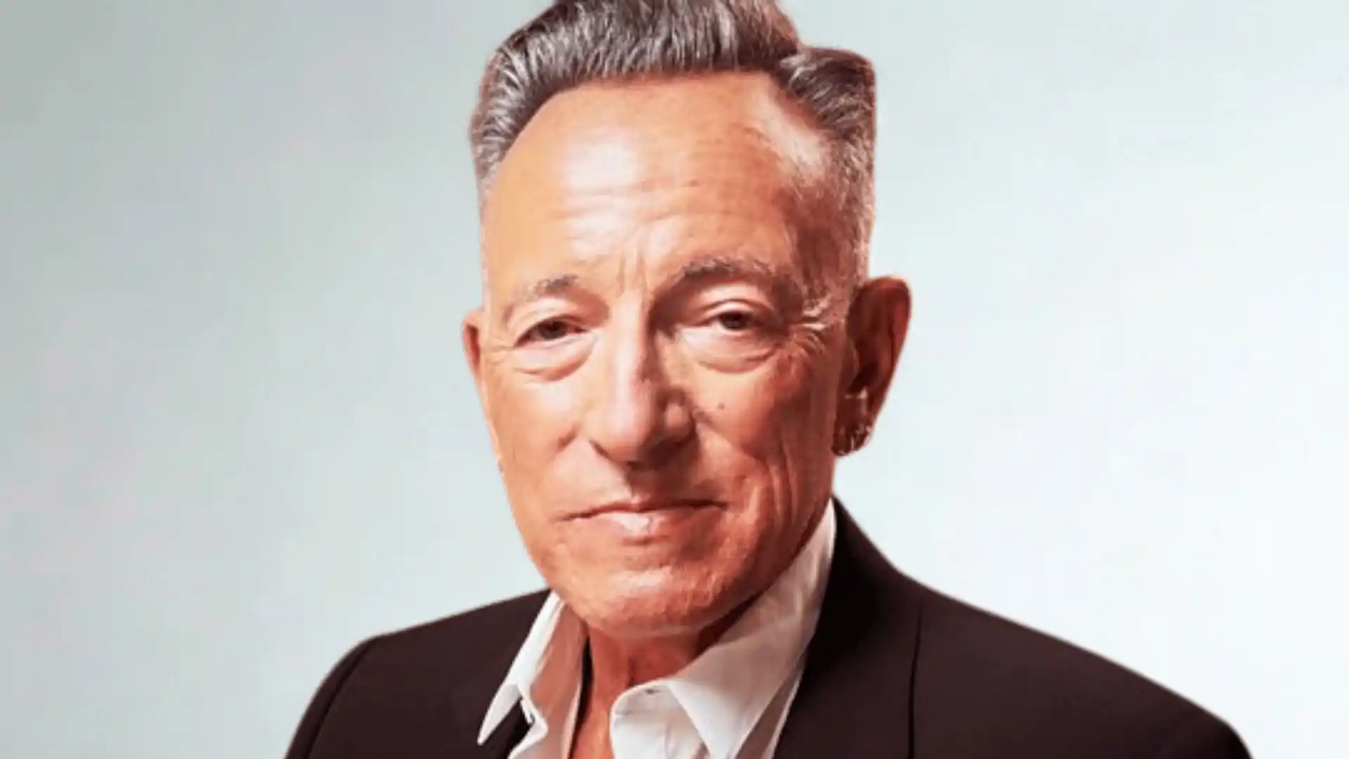 Close-up portrait of Bruce Springsteen wearing a dark suit and open white shirt.