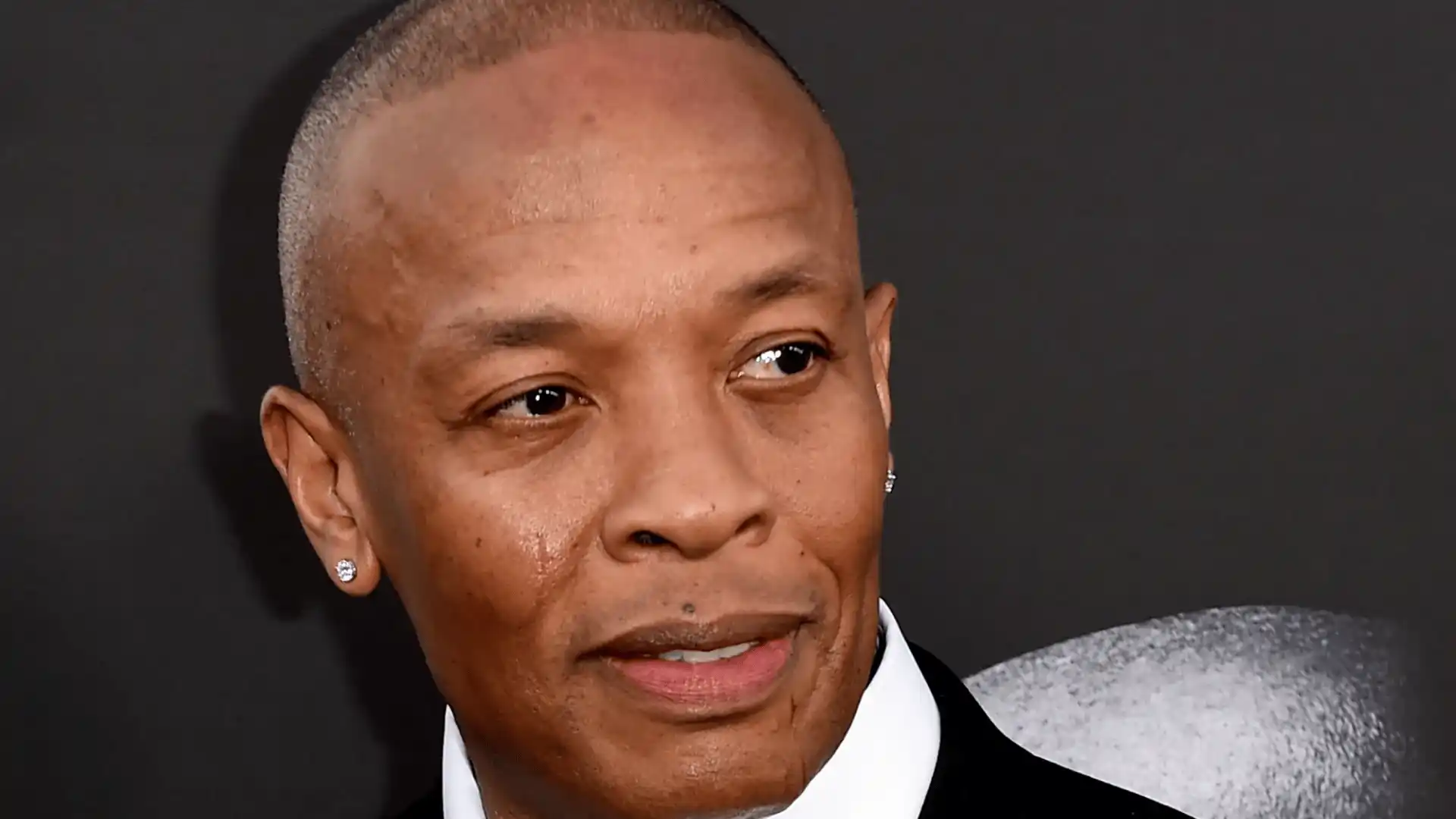 Close-up portrait of Dr. Dre in a suit with earring against dark background.