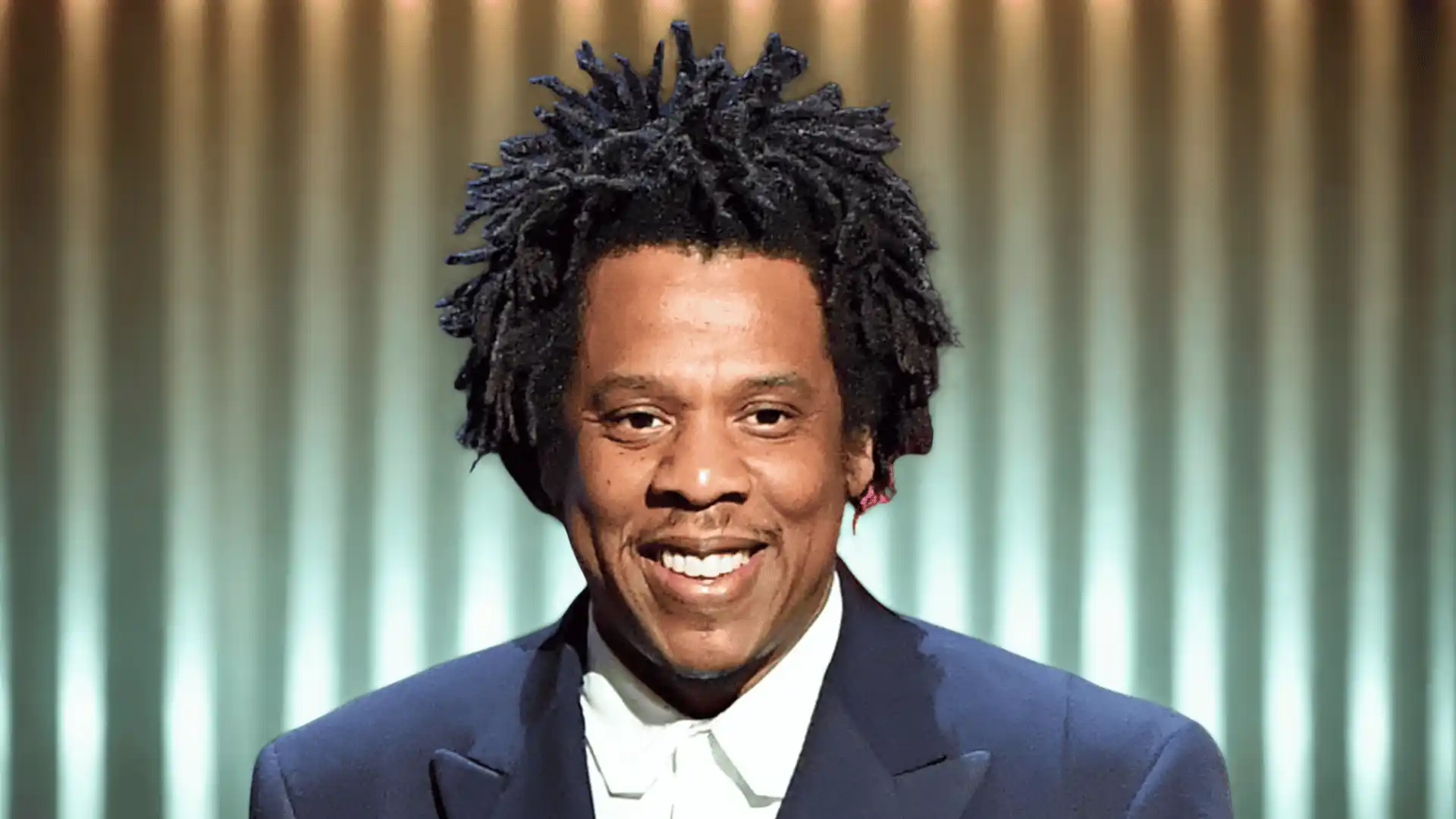 Close-up portrait of Jay-Z wearing a suit, smiling against a dark background.
